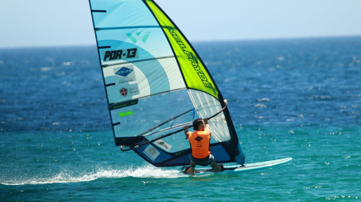 Windsurfer gliding on turquoise waters with green sail against ocean horizon.