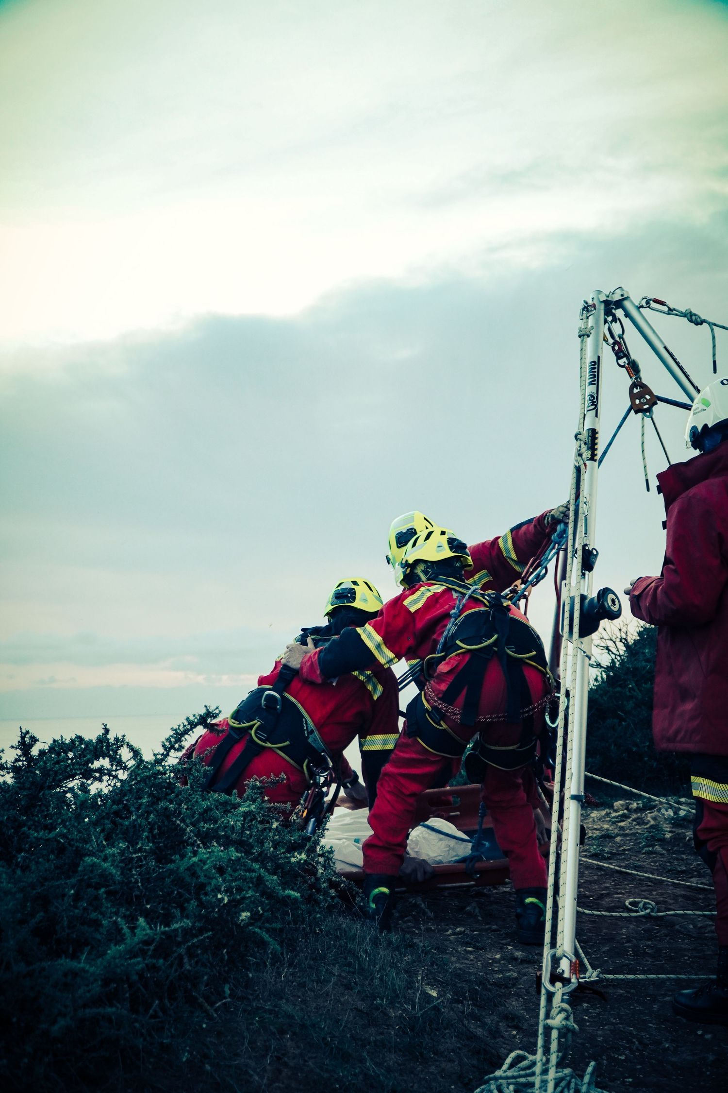 Emergency rescue technician in red gear climbing a metal tower structure during a low-light training exercise.