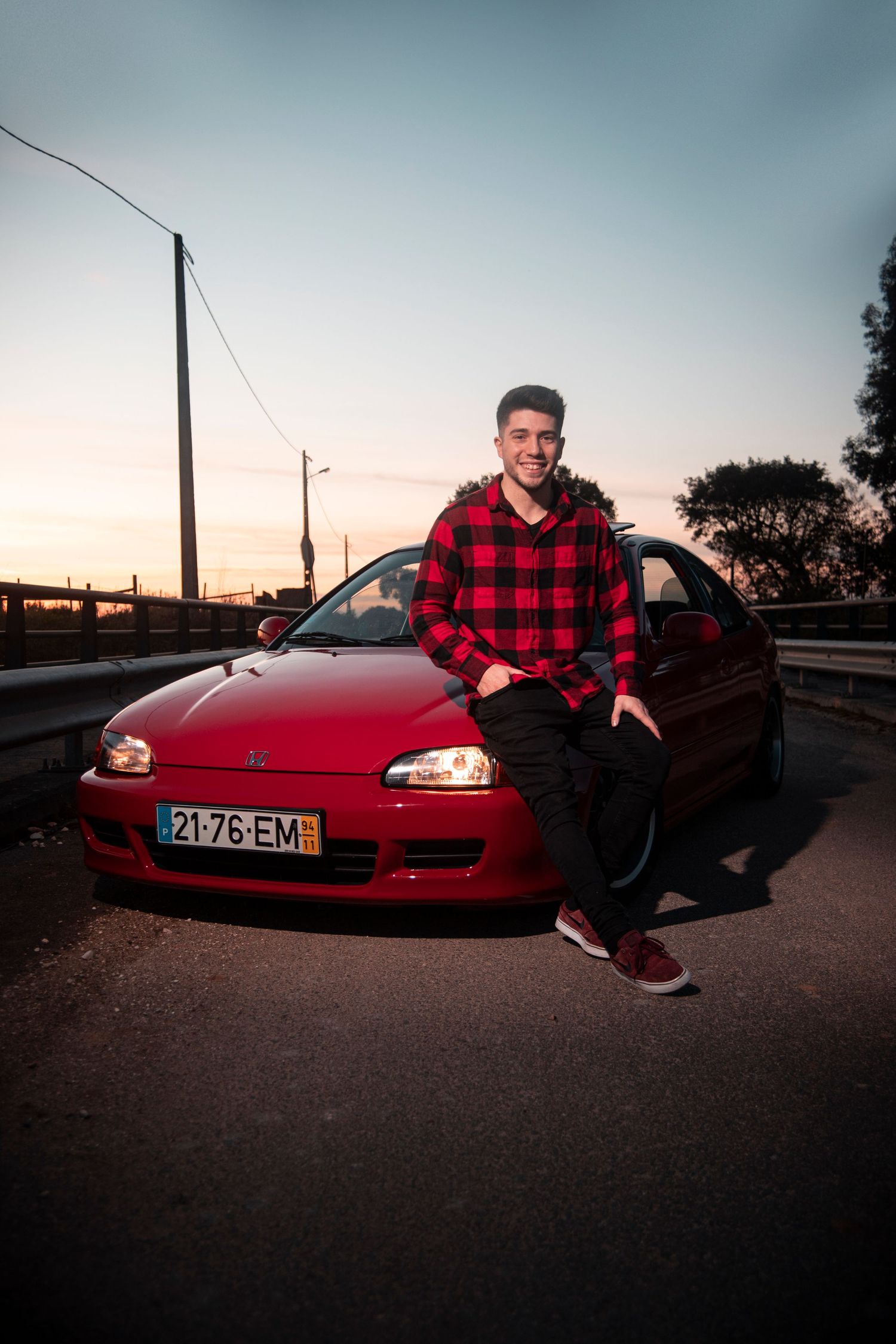 Red sports car parked at sunset with utility poles and trees in background.