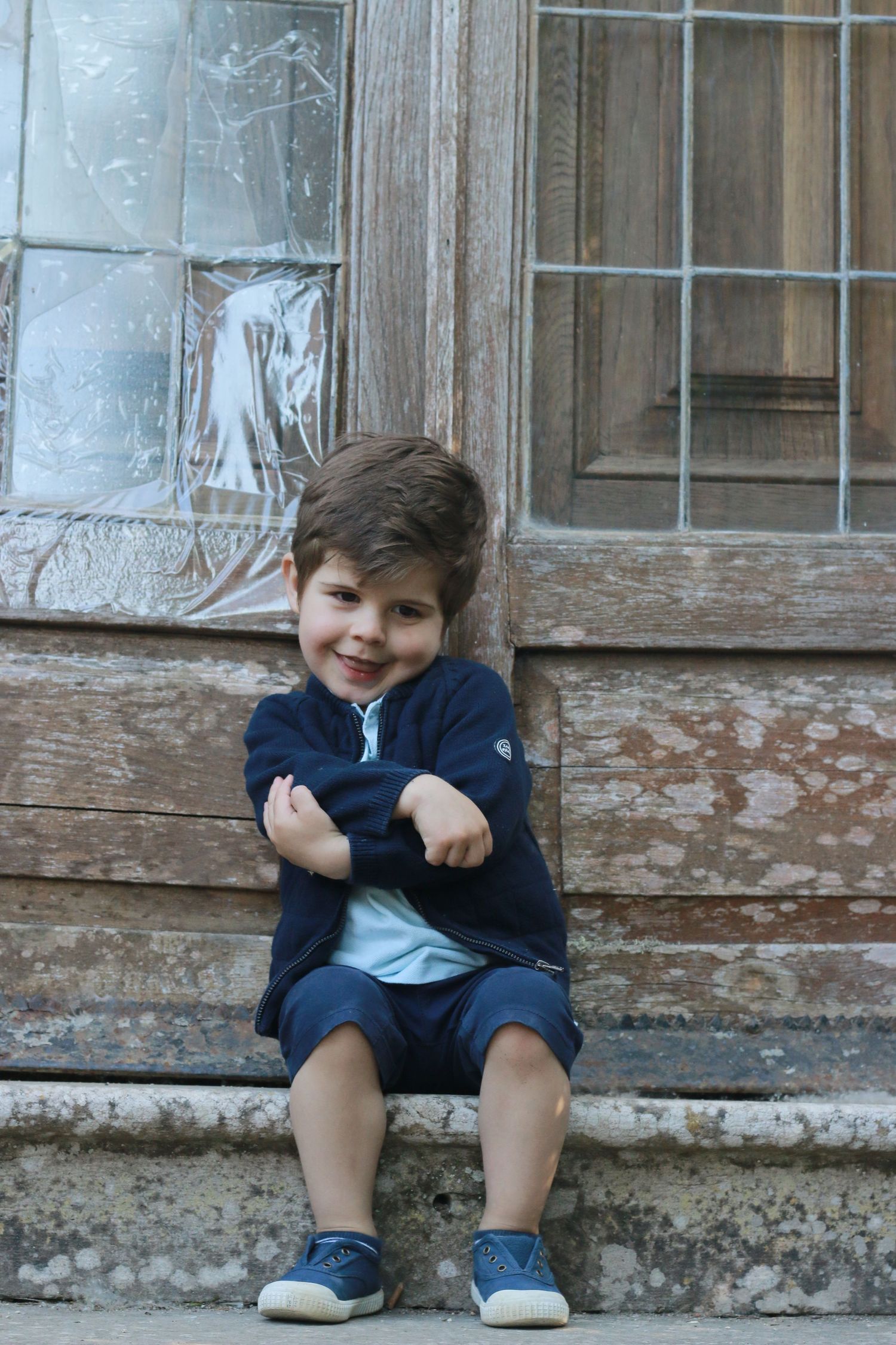 Child in navy sweater sits casually on rustic stone steps.