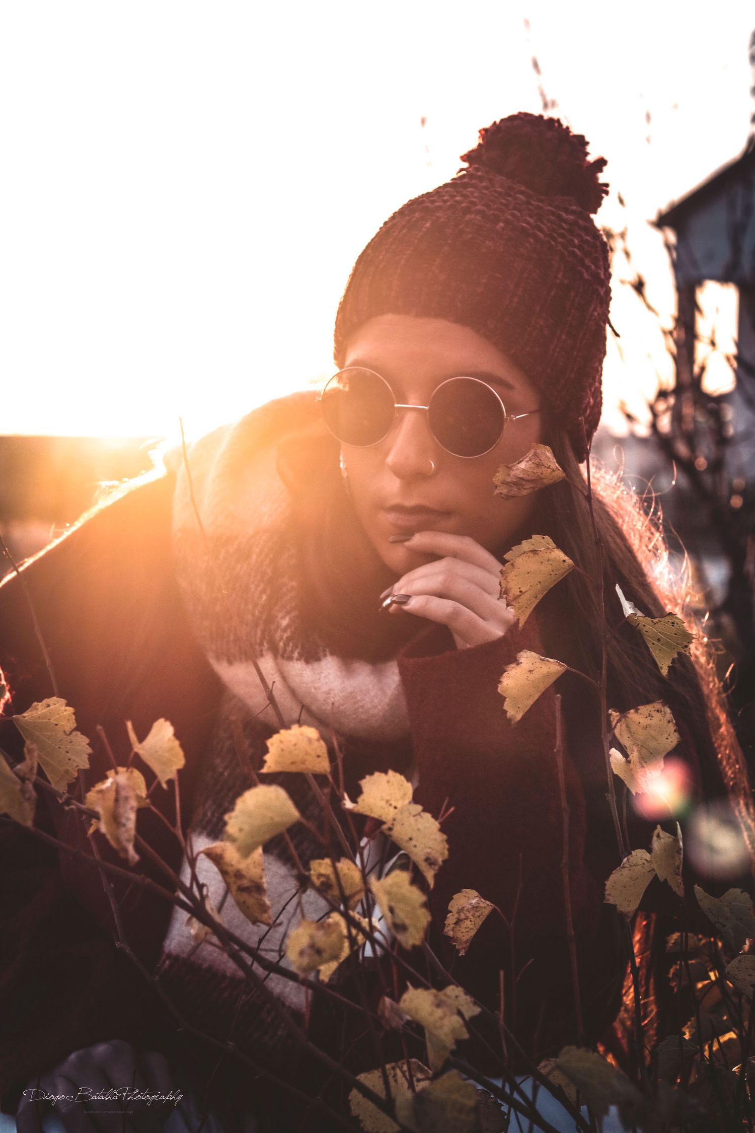 Artistic portrait at sunset with round sunglasses and knit beanie among delicate yellow flowers in warm golden light.