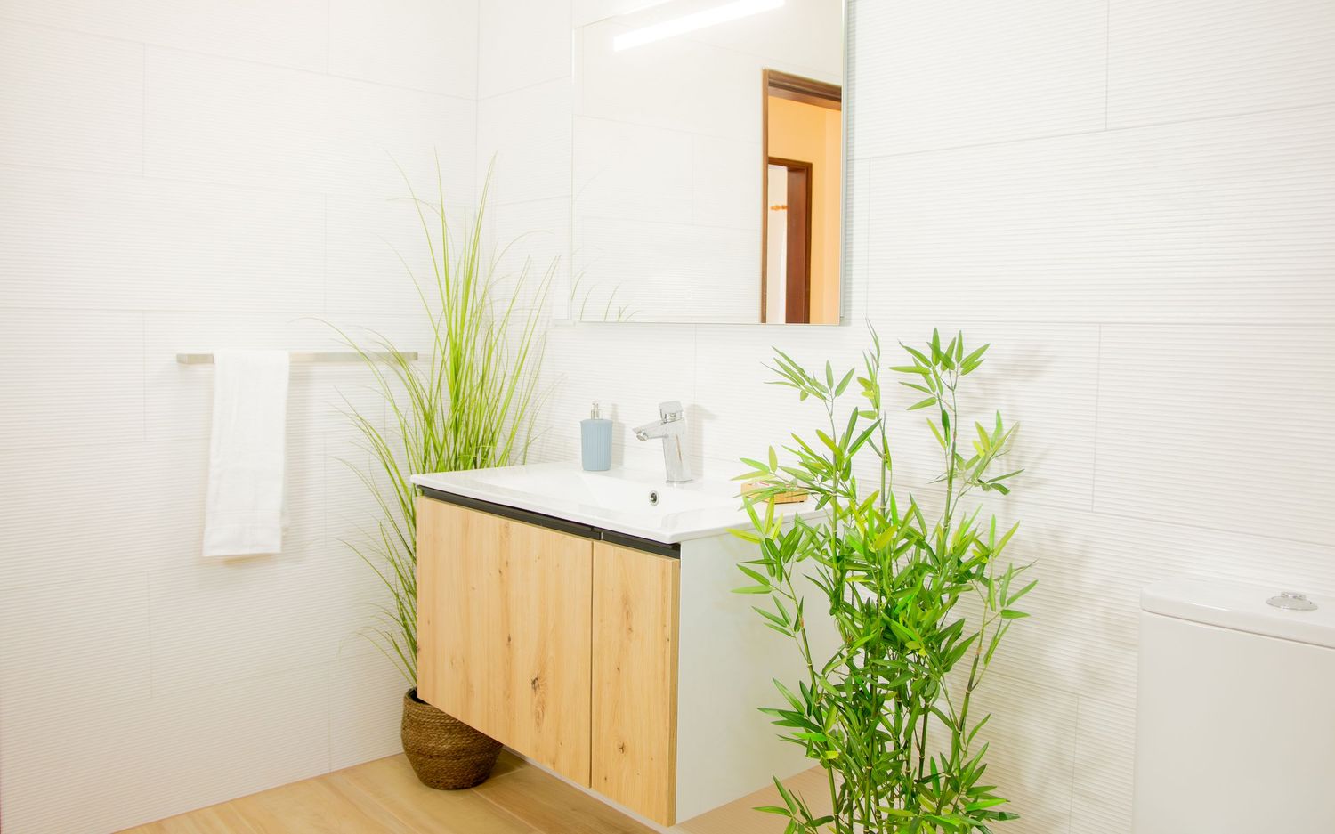 Modern bathroom interior with wooden vanity, white countertop, and decorative bamboo plant creating a spa-like atmosphere.