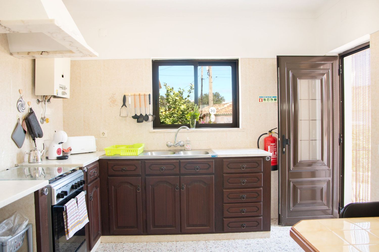 Modern kitchen interior with dark wood cabinets, stainless steel appliances and window overlooking outdoor greenery.