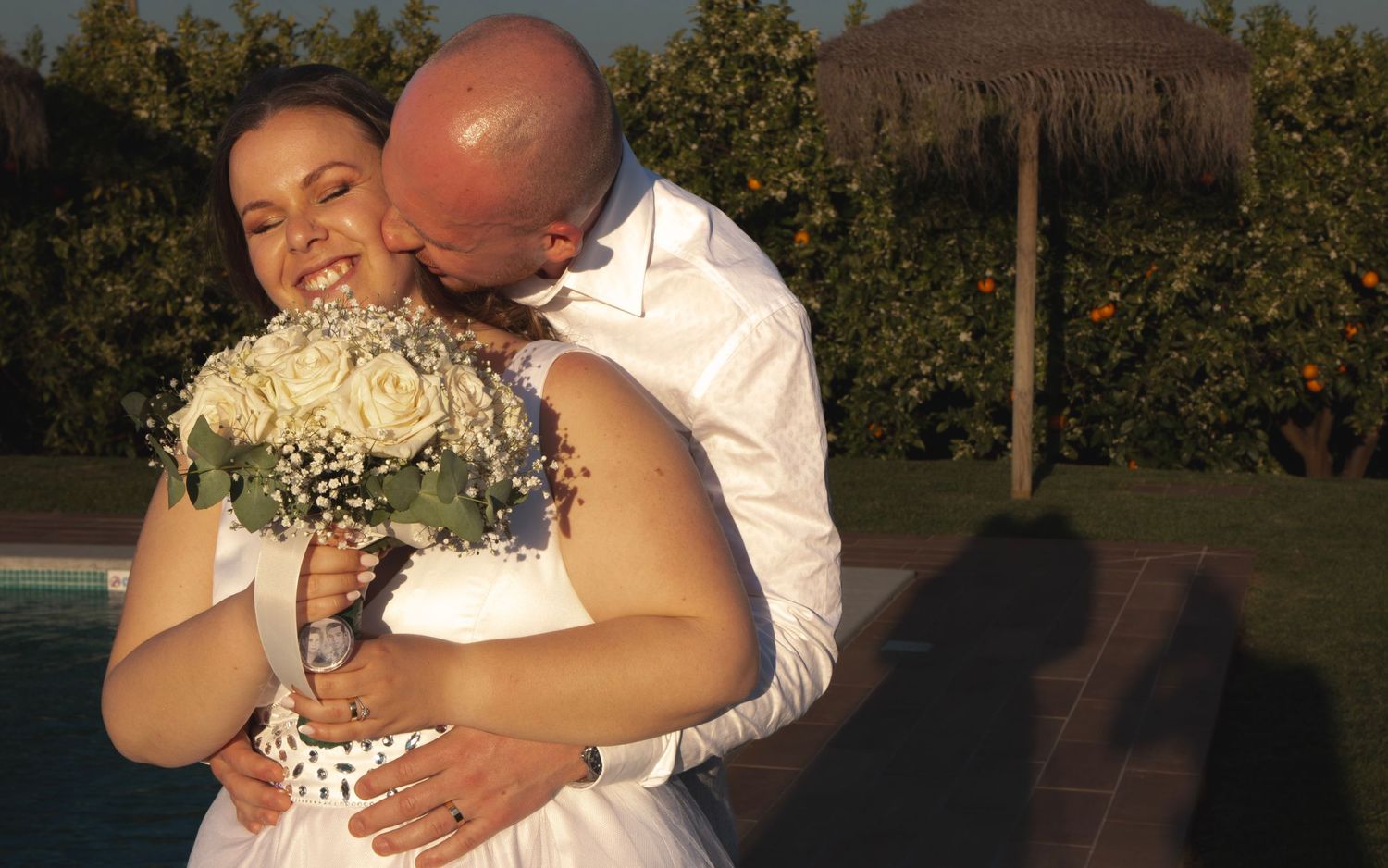 A joyful wedding moment outdoors with the bride holding a bouquet during sunset.