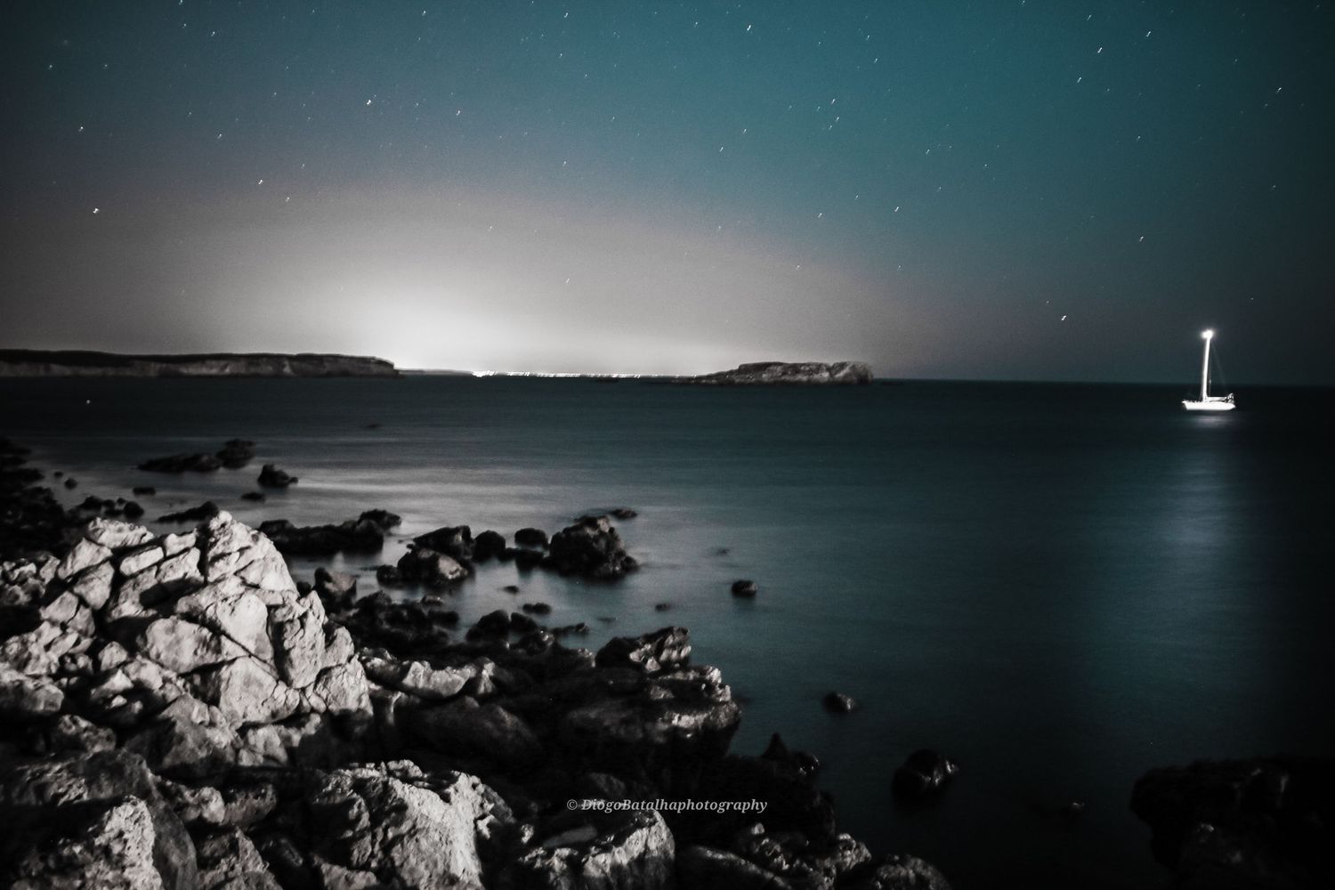 Coastal night landscape with stars and rocky cliffs overlooking the ocean.
