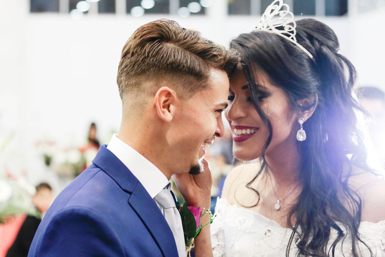 A couple shares an intimate moment at their wedding ceremony wearing a navy suit and white gown with tiara.