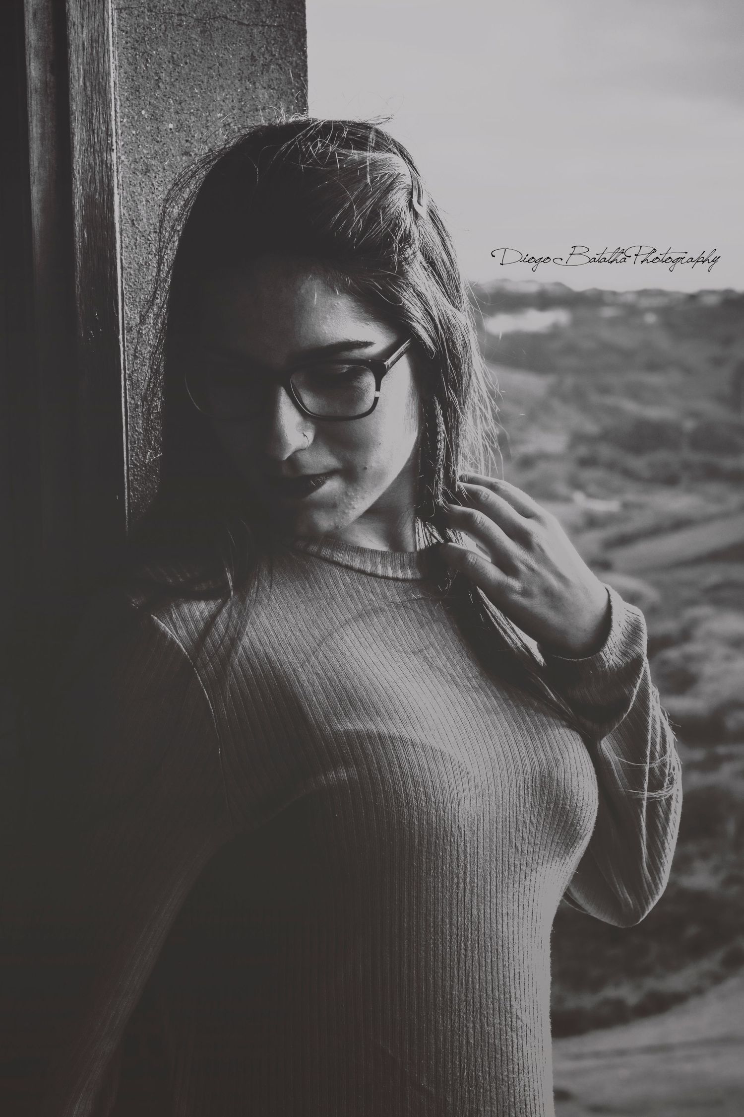 Moody black and white portrait featuring someone in glasses wearing a sweater, shot against a window.