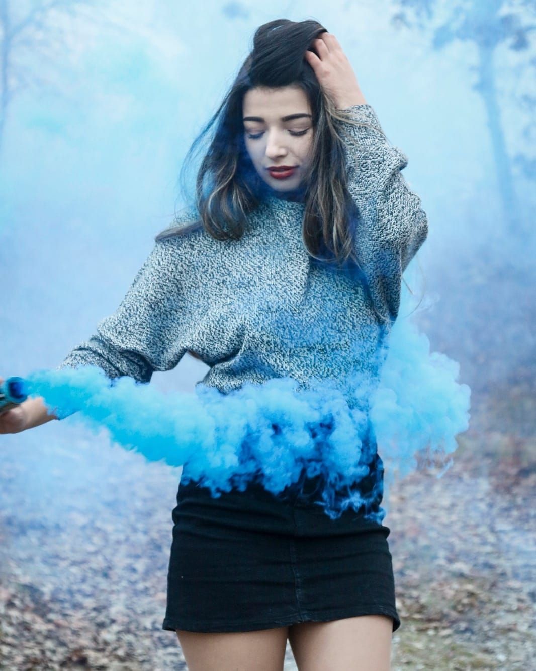 Artistic portrait with blue smoke bomb effect against misty forest background.