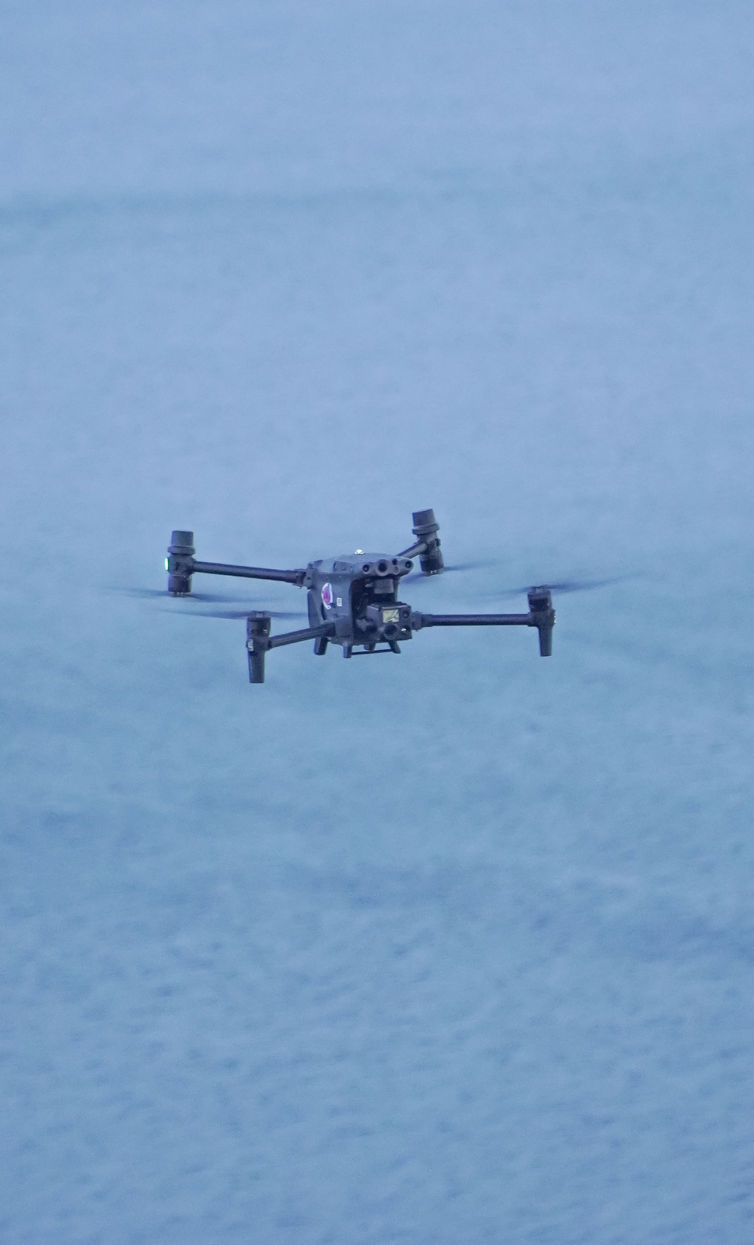 A black quadcopter drone hovers in the air against a misty blue background.