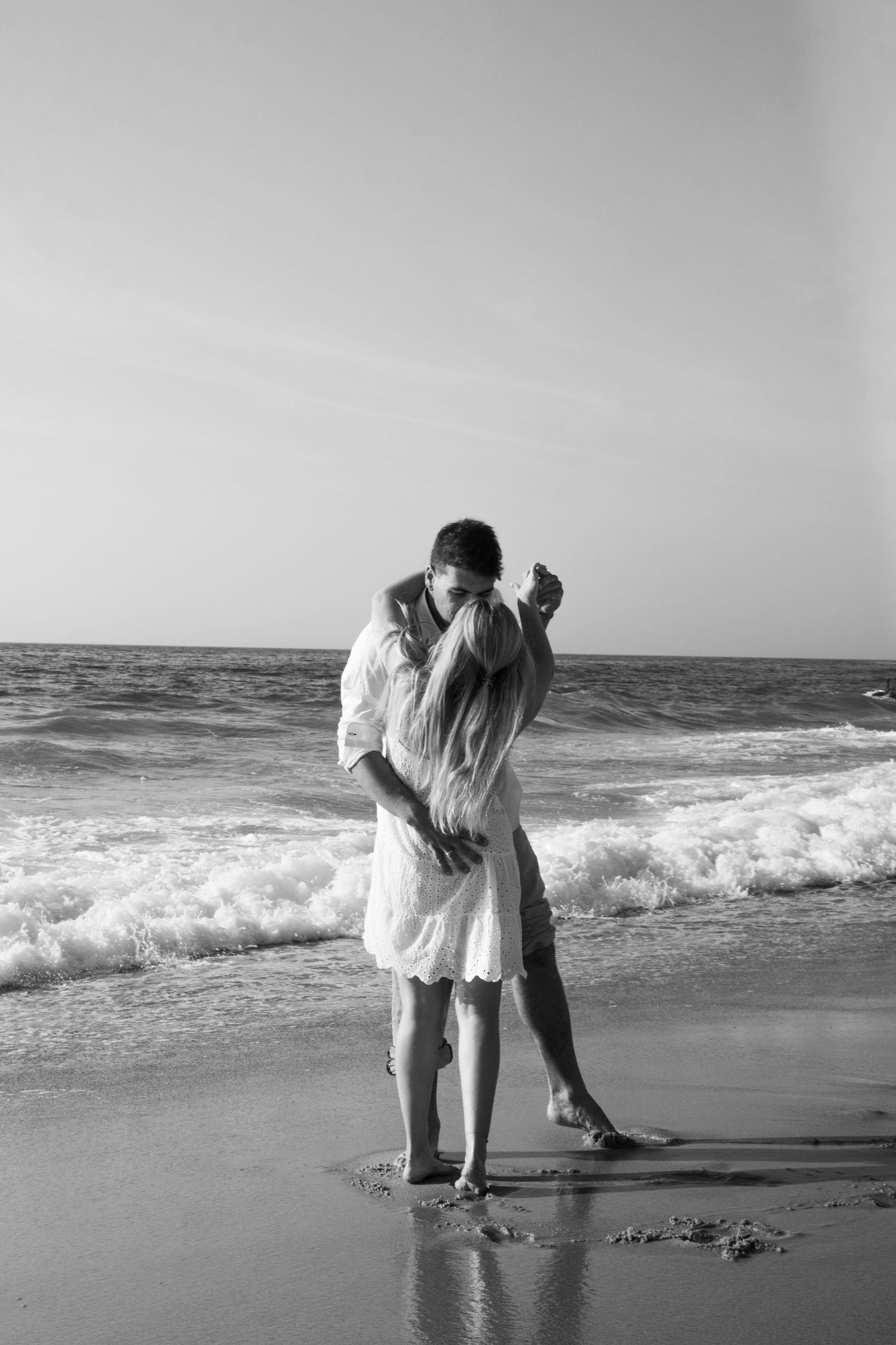 A romantic black and white photo sequence of a couple embracing on a beach with crashing waves in the background.