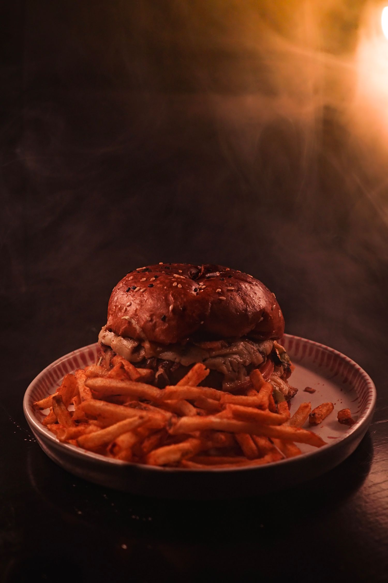 Close-up of french fries and burger served on a white plate in dark ambiance.