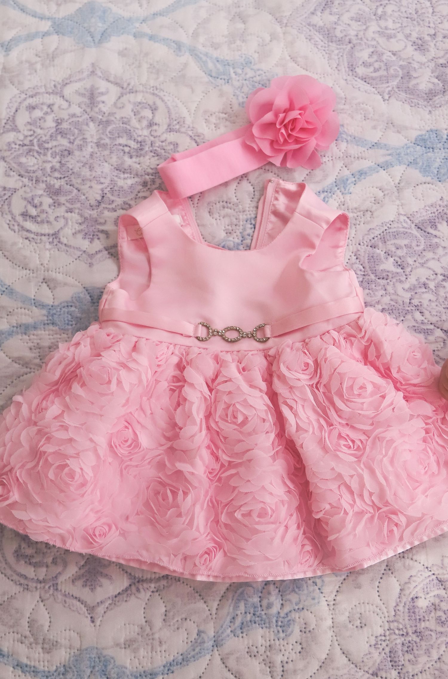 Pink rosette dress with matching headband displayed on textured gray and white background.