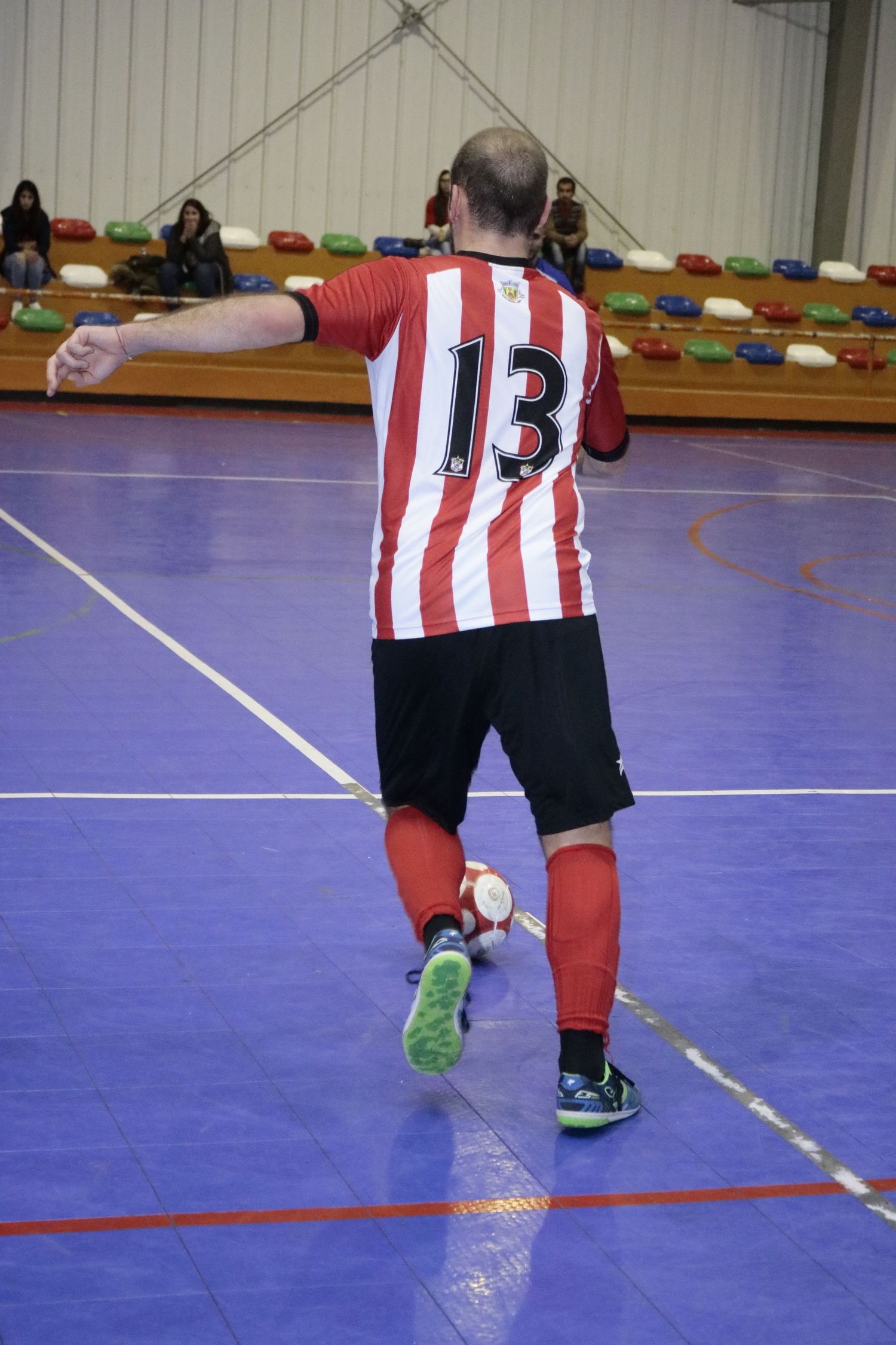 Soccer player wearing red and white striped jersey number 13 plays indoor futsal on purple court.