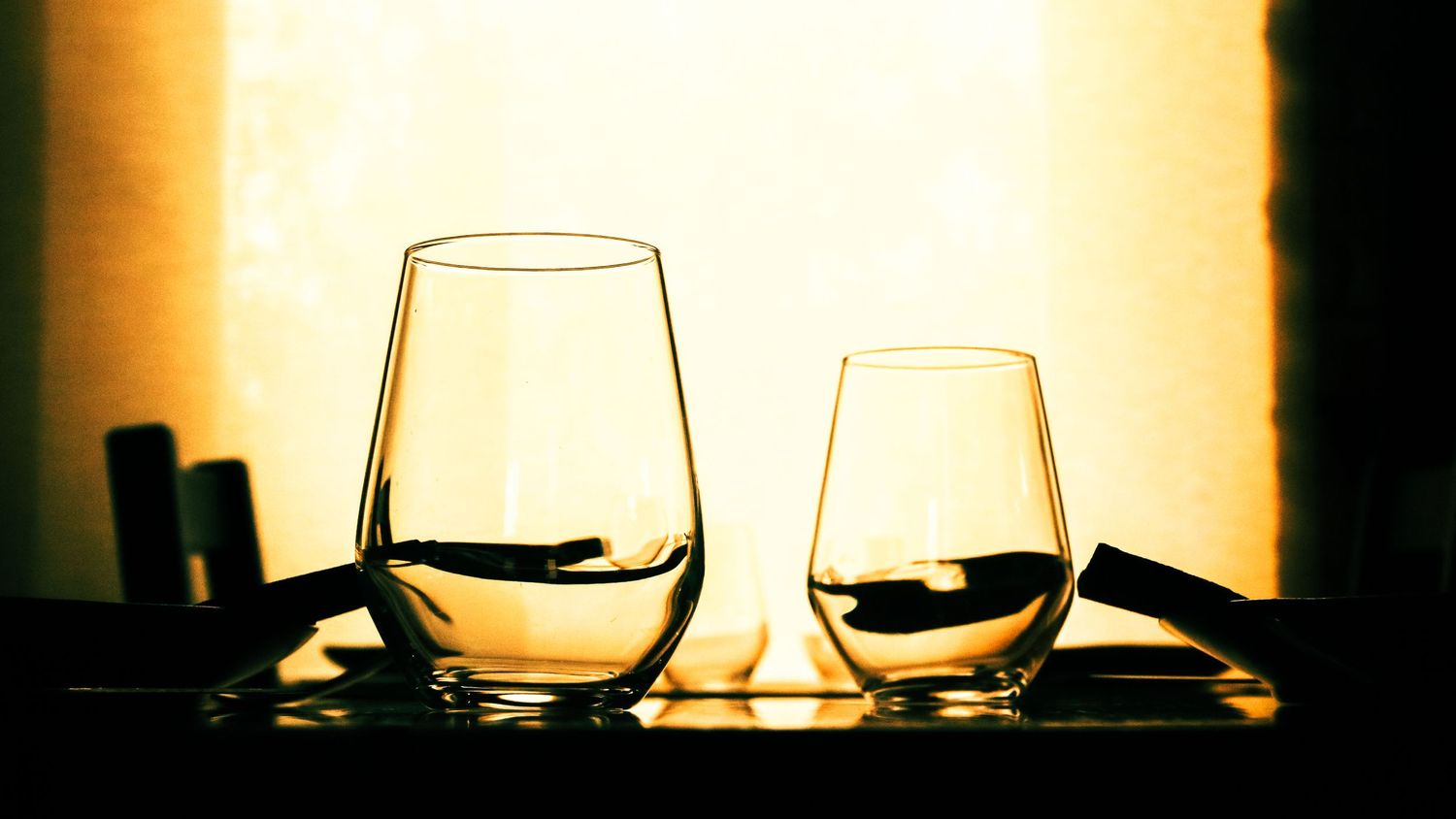 Two wine glasses silhouetted against warm backlit background.