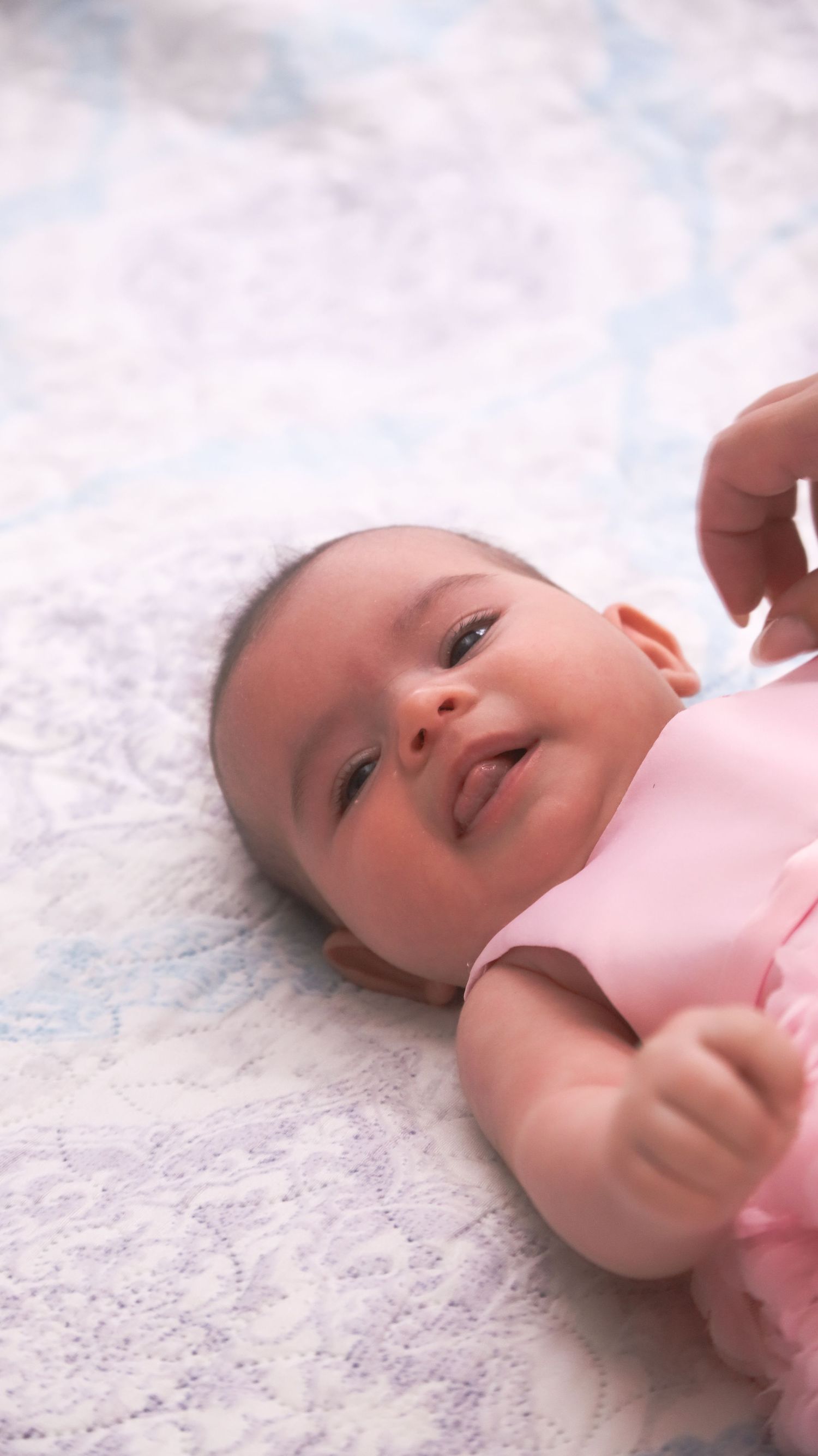 Sweet moment of young infant wearing pink outfit lying on patterned fabric.