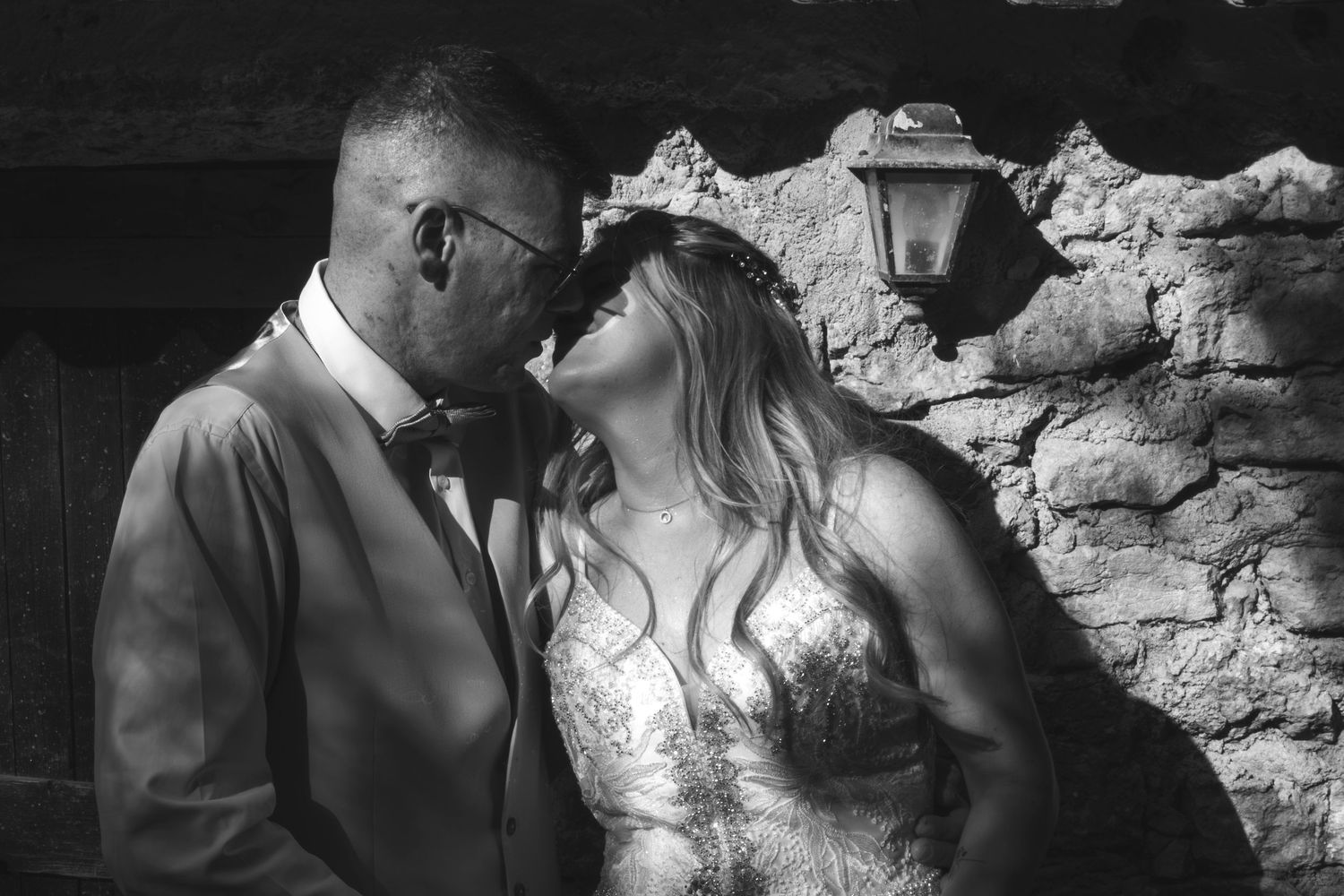 Black and white photo of a bride and groom sharing a romantic moment near a rustic stone wall.