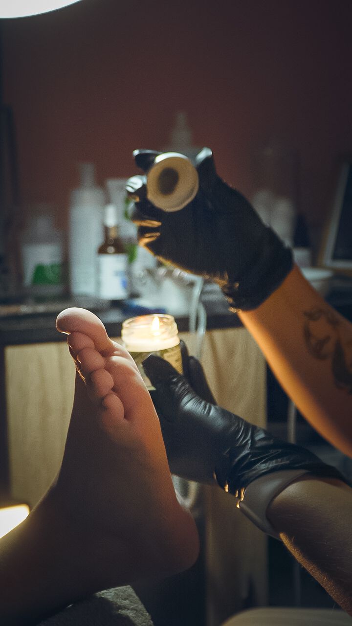 Professional podiatrist in black gloves inspects a patient's foot during treatment using specialized equipment.