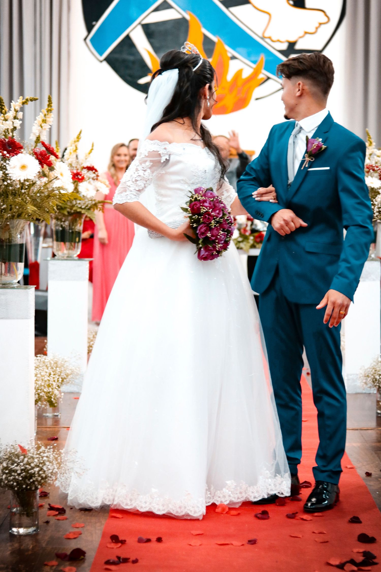 Wedding ceremony with couple in traditional attire on red carpet with floral decorations.