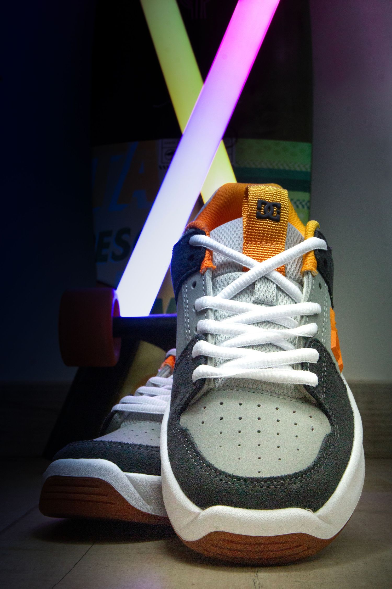 DC sneaker illuminated by colorful neon lights against dark background.