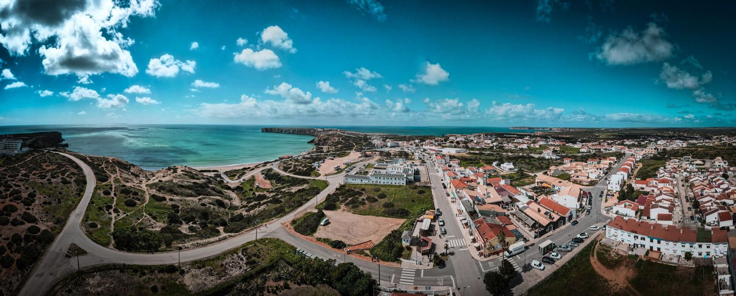 Panoramic aerial view of a coastal town with winding roads and white buildings overlooking the turquoise ocean.