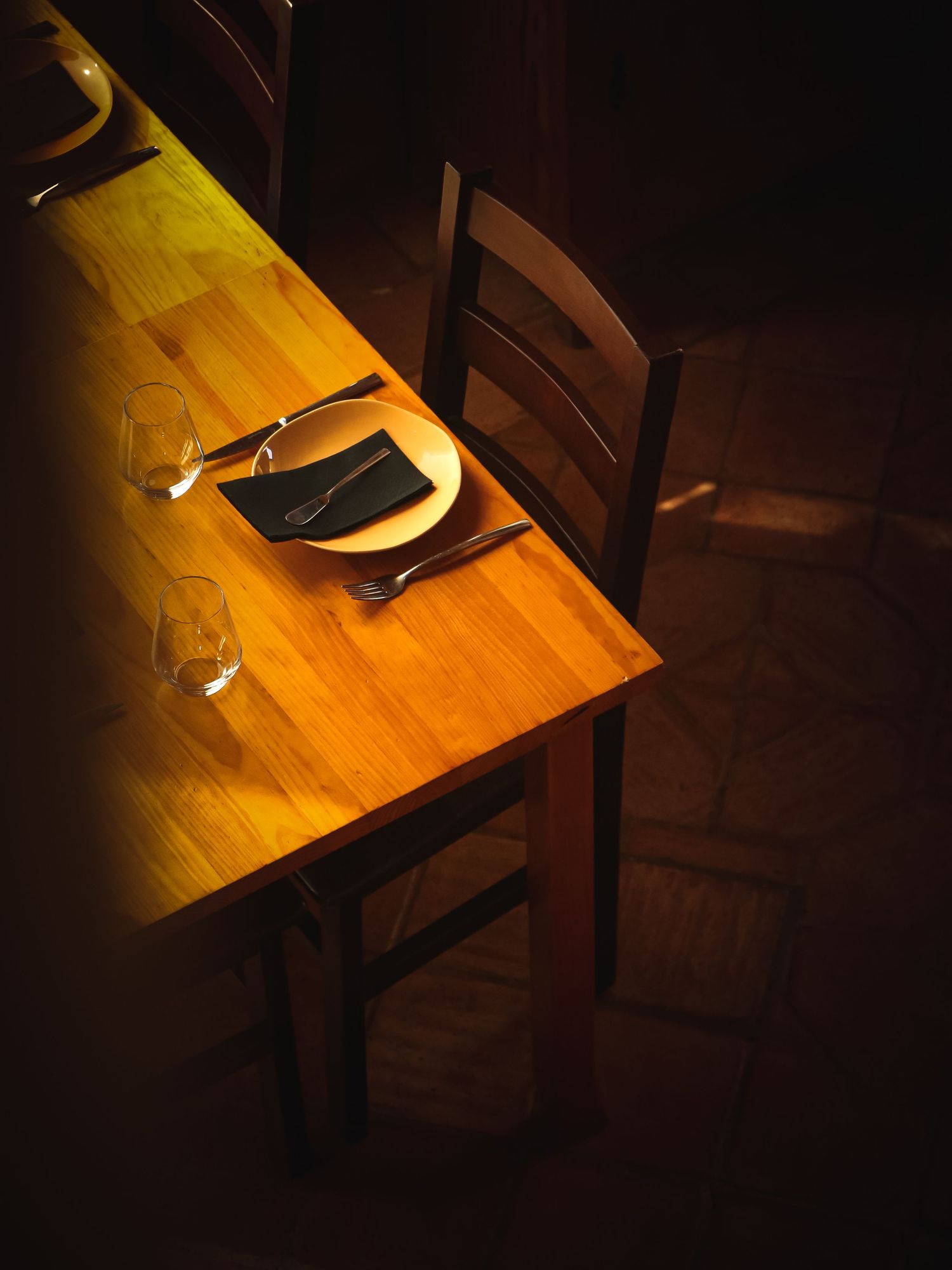 Place setting on wooden table illuminated by dramatic spotlight.