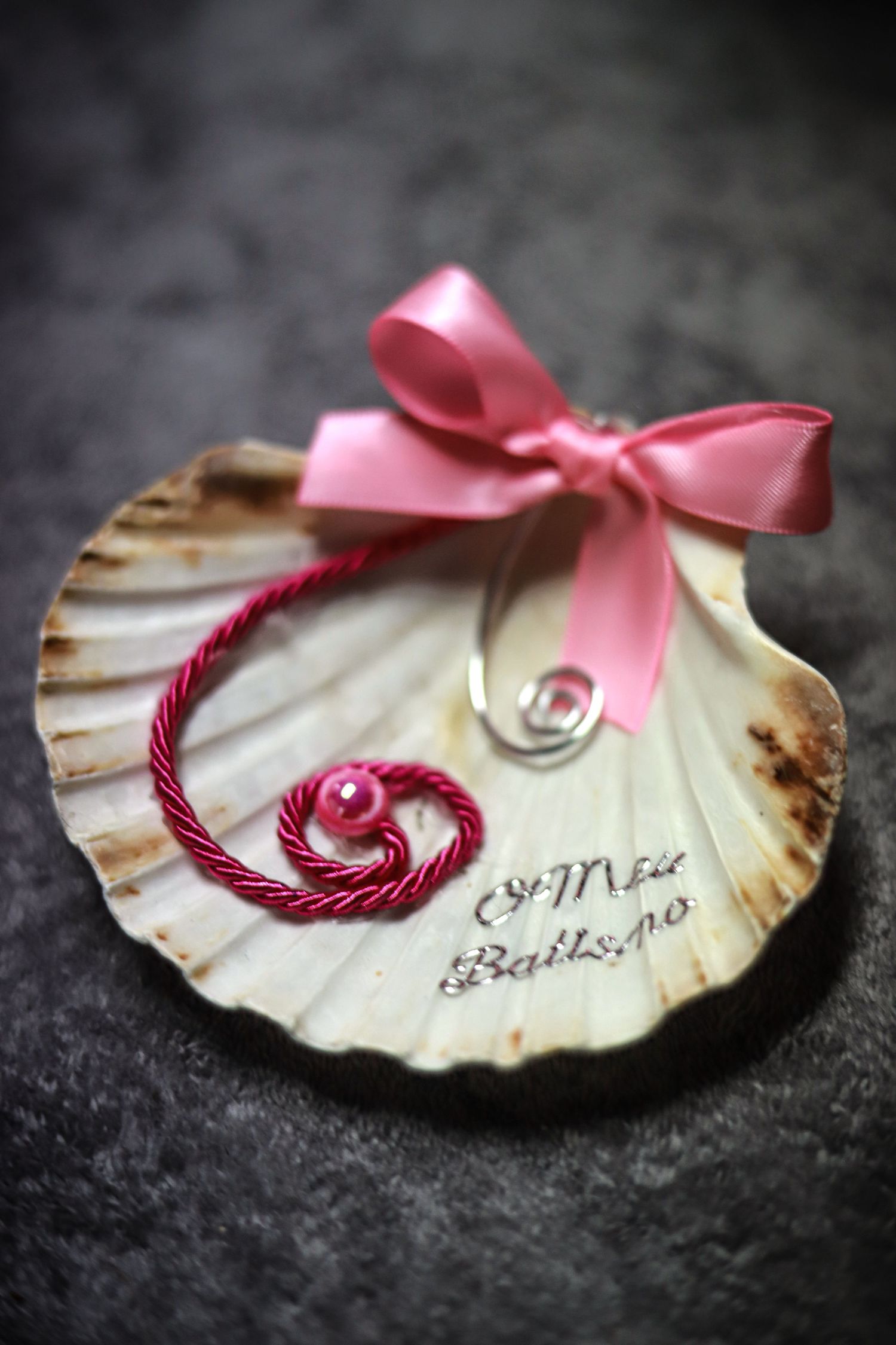 Decorative seashell with pink ribbon bow and burgundy twine forming a heart shape.