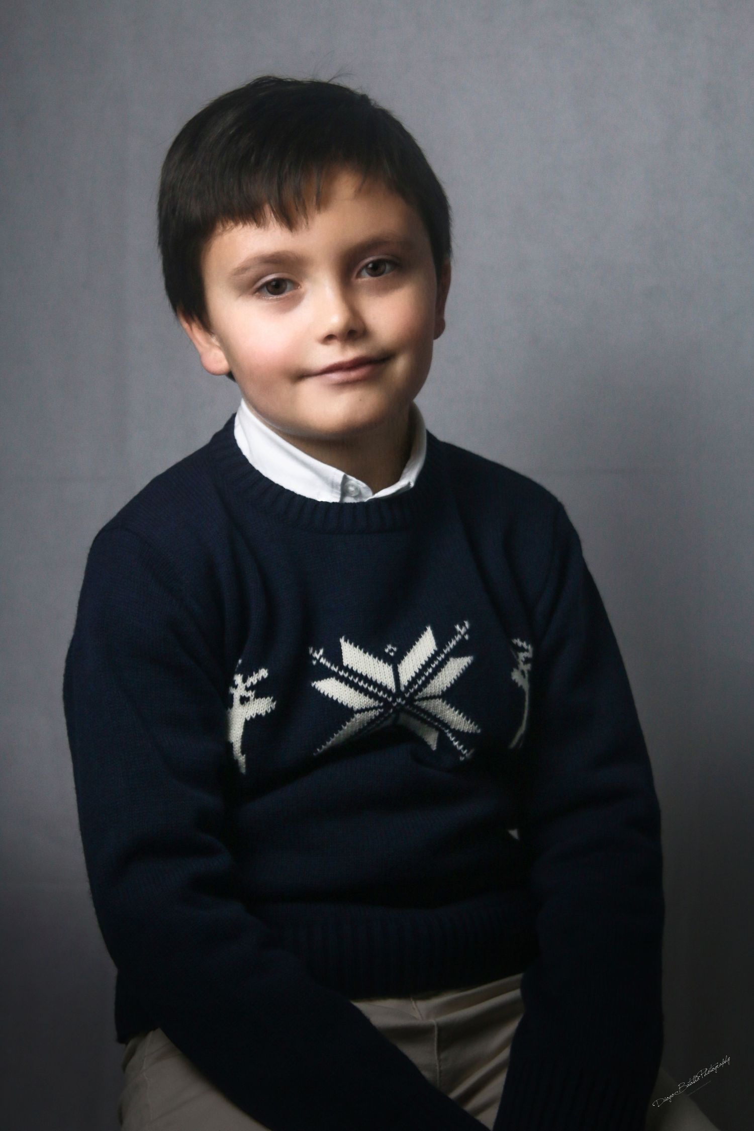 Studio portrait of young person in navy sweater with festive snowflake pattern against grey background.