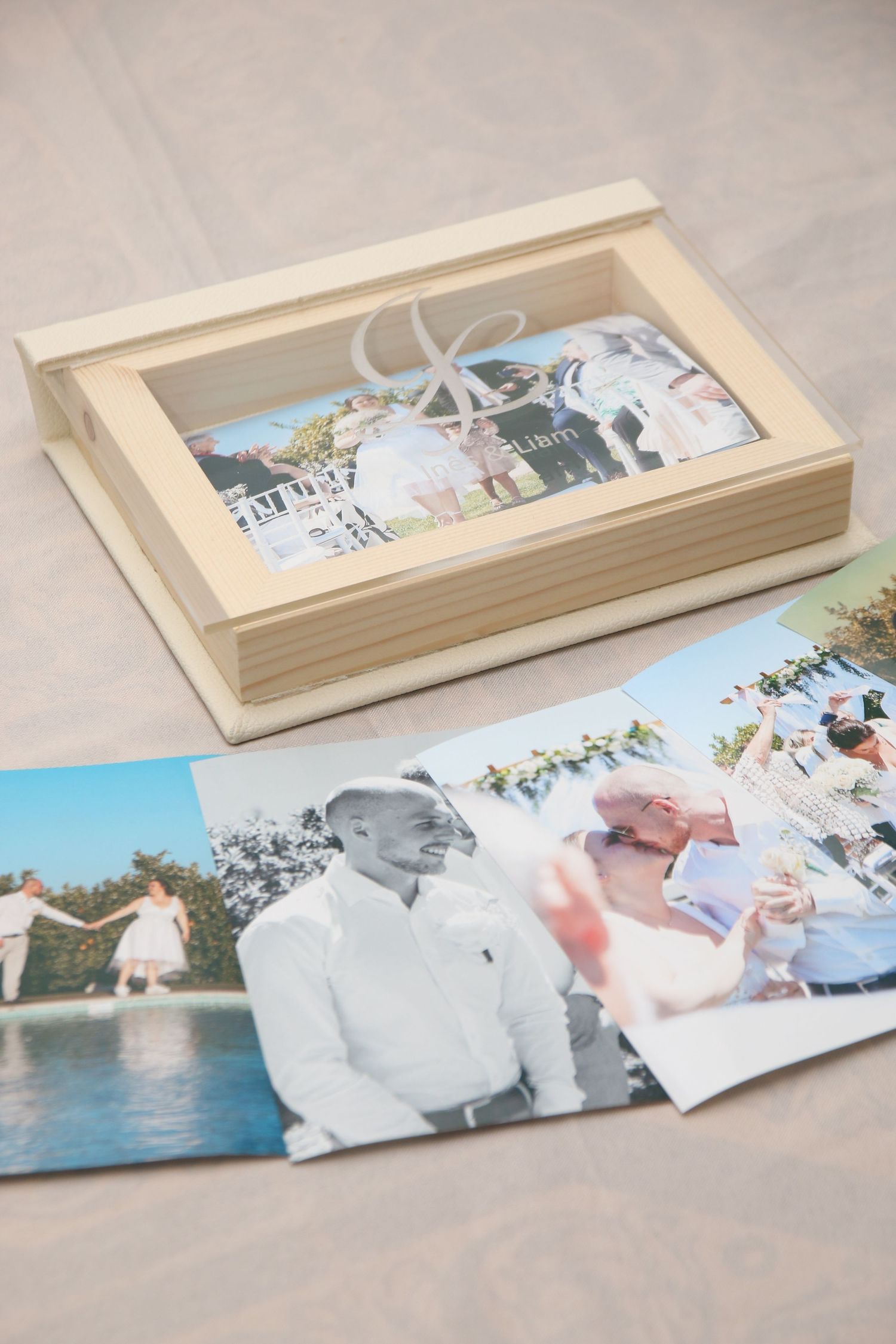 A wooden keepsake box displaying wedding photos with matching prints laid beside it.