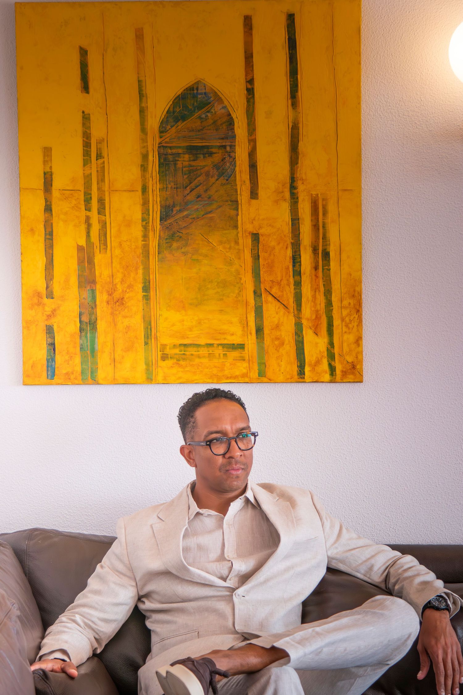A multi-panel sequence showing someone in a white shirt and glasses seated on a couch with yellow artwork on the wall.