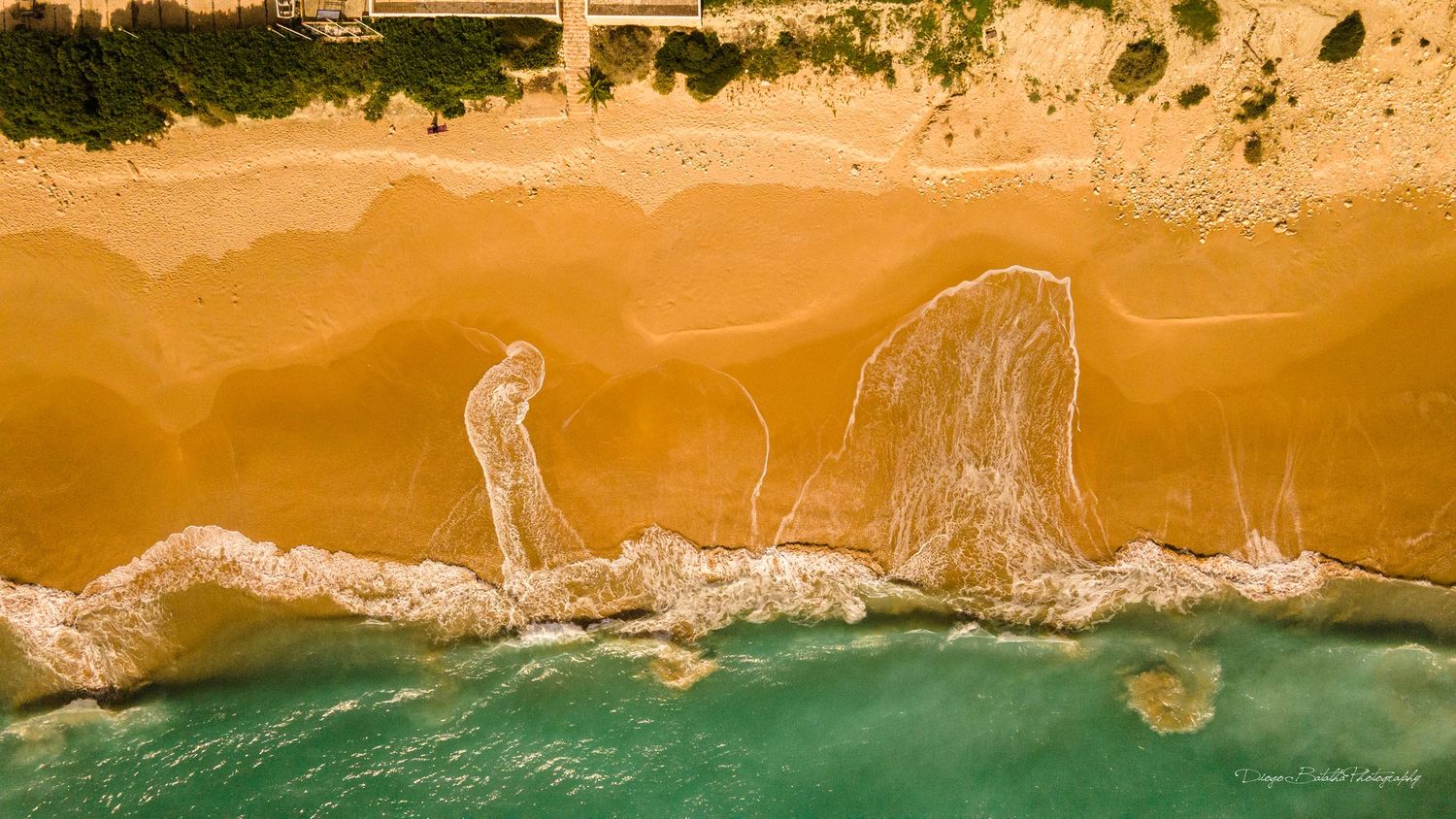 Aerial view of sandy beach coastline with turquoise waters and rolling waves.