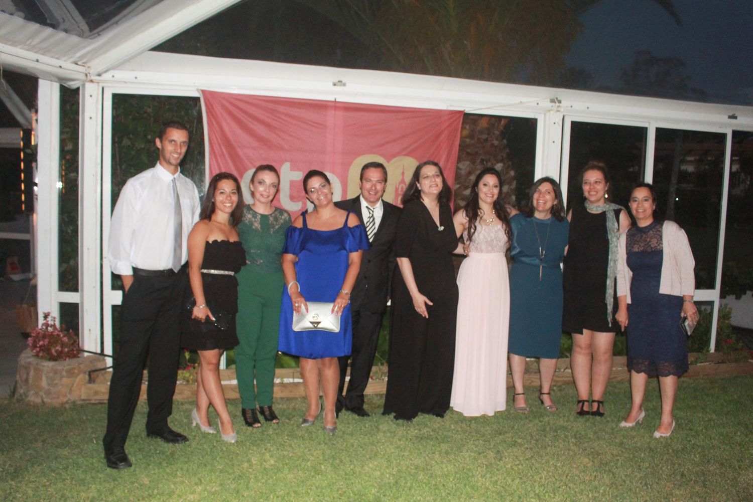Large group of wedding guests posing together under outdoor event tent at night.