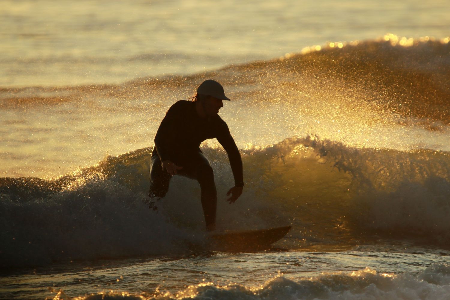Silhouette of surfer riding wave at sunset with golden water spray.