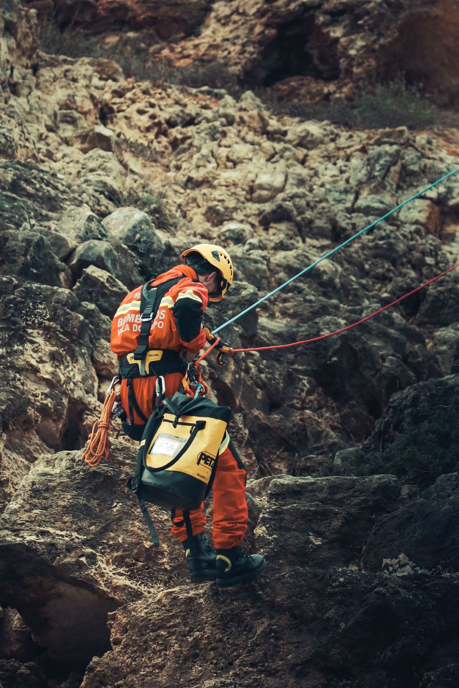 Rock climber in orange safety gear navigating challenging terrain with specialized equipment and ropes.