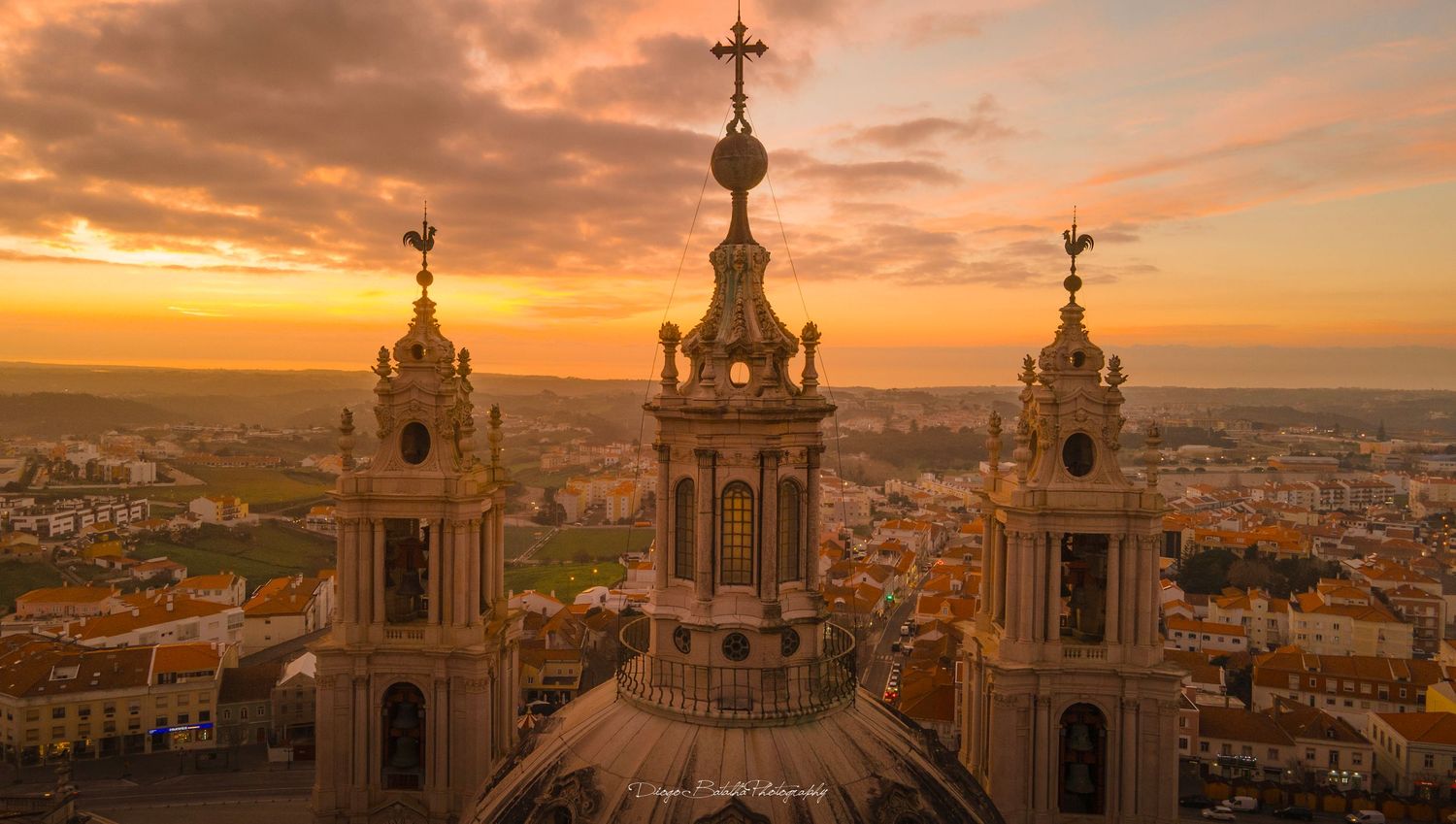 Historic church spires silhouetted against dramatic orange sunset sky over cityscape.