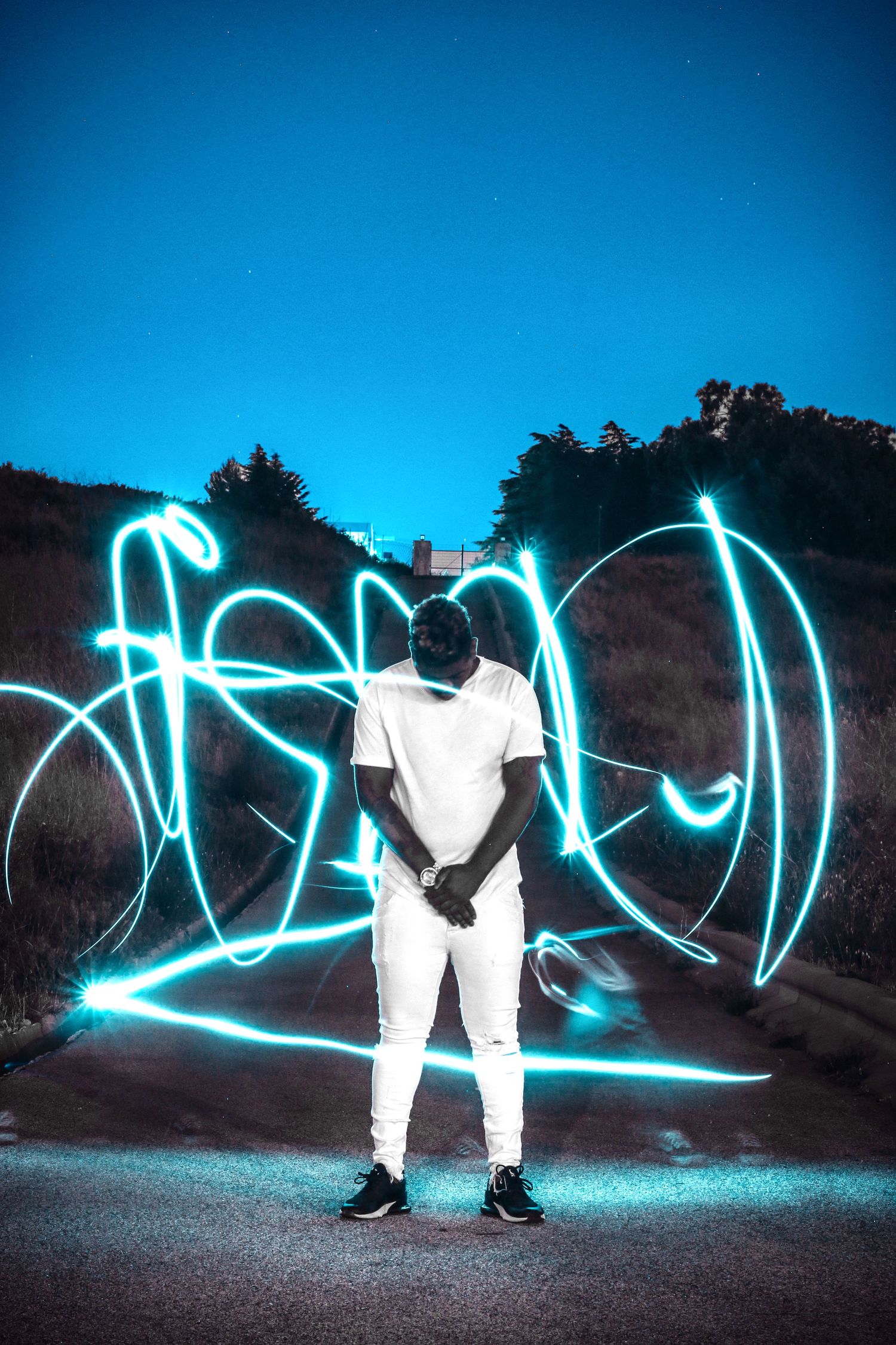 Silhouette stands before glowing blue light painting trails at night creating an ethereal long exposure effect.