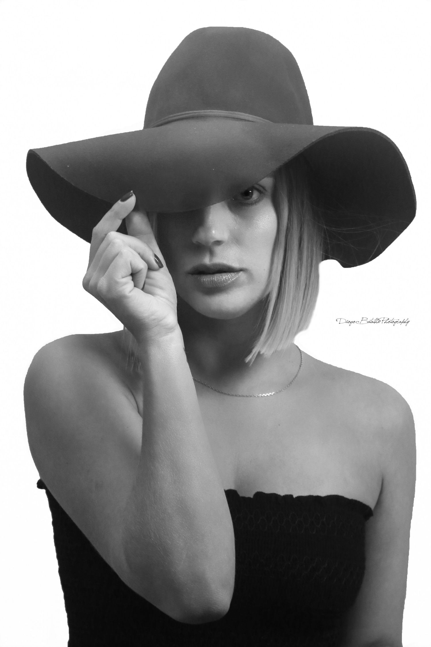 A black and white fashion portrait featuring a dramatic wide-brimmed hat and strapless black top.