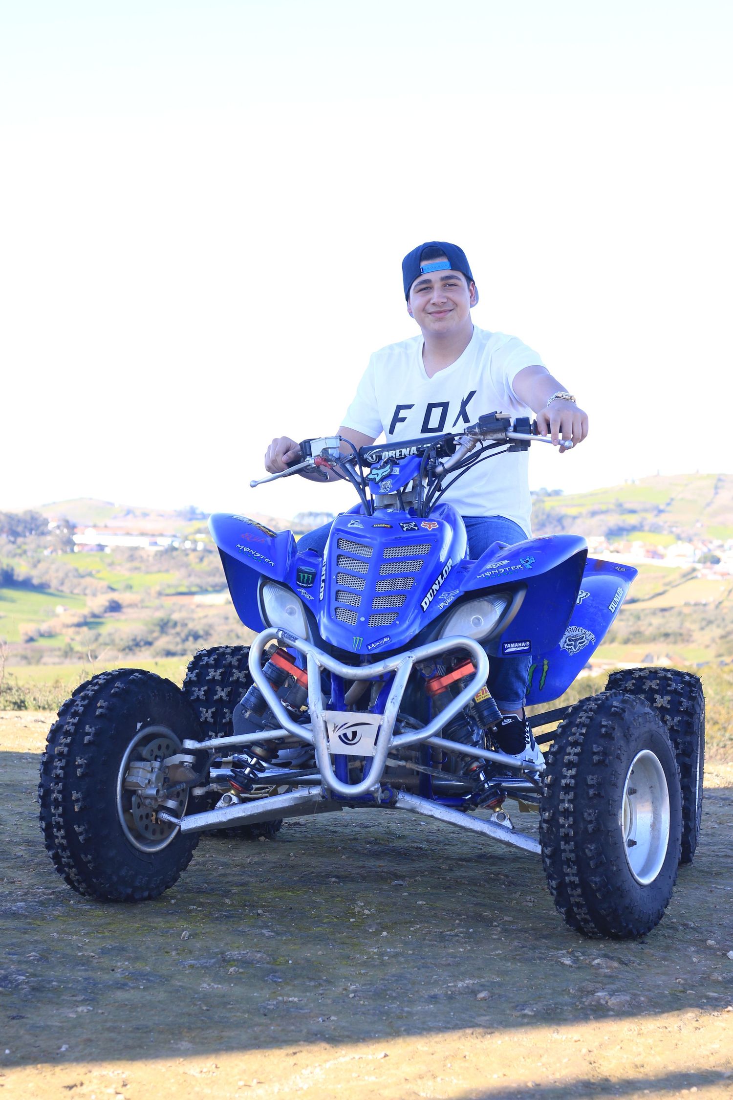Person riding a blue quad bike ATV on outdoor terrain wearing FOX gear.