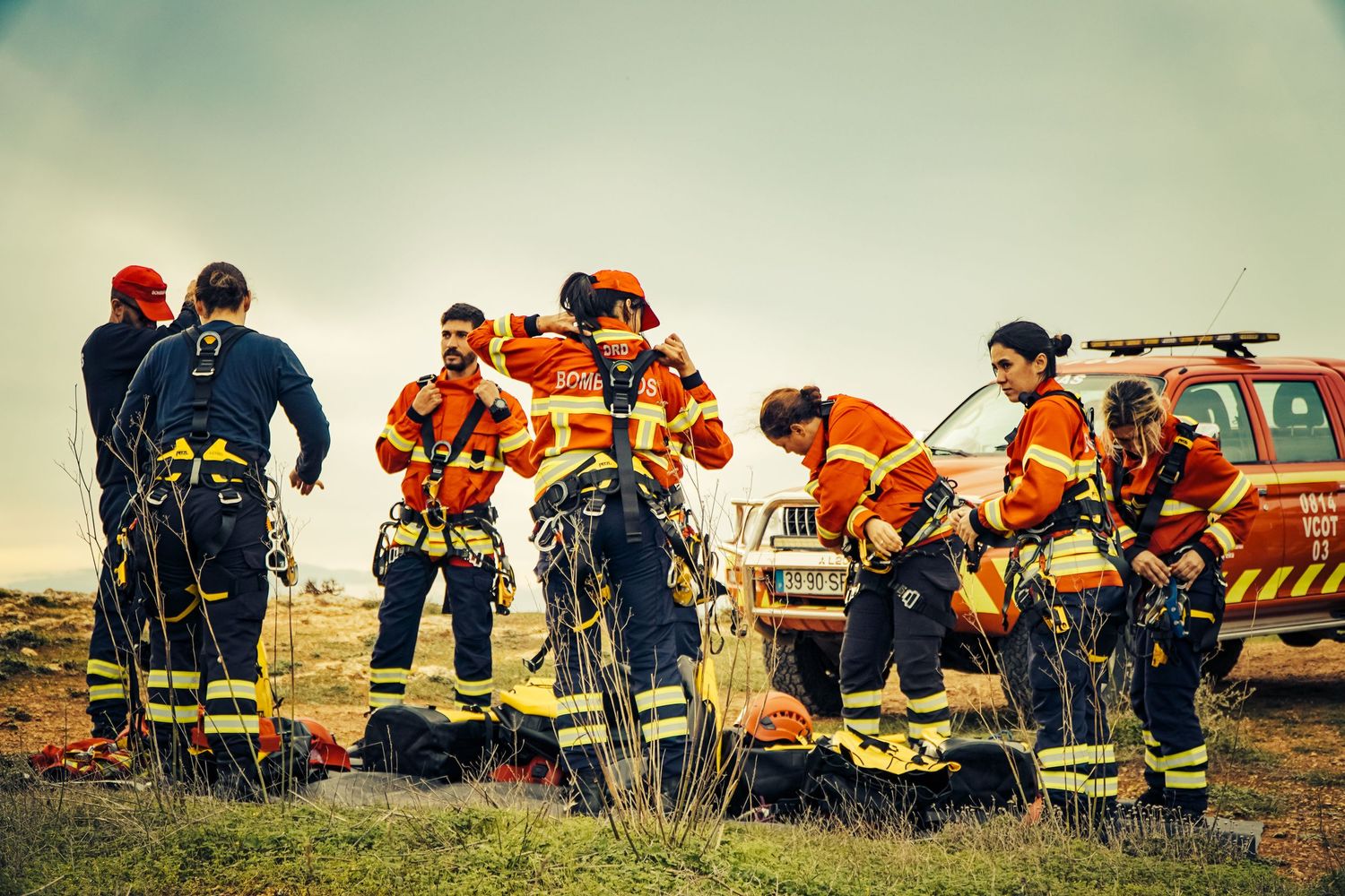 Search and rescue team members in orange safety gear gather on a hillside during an emergency response operation.