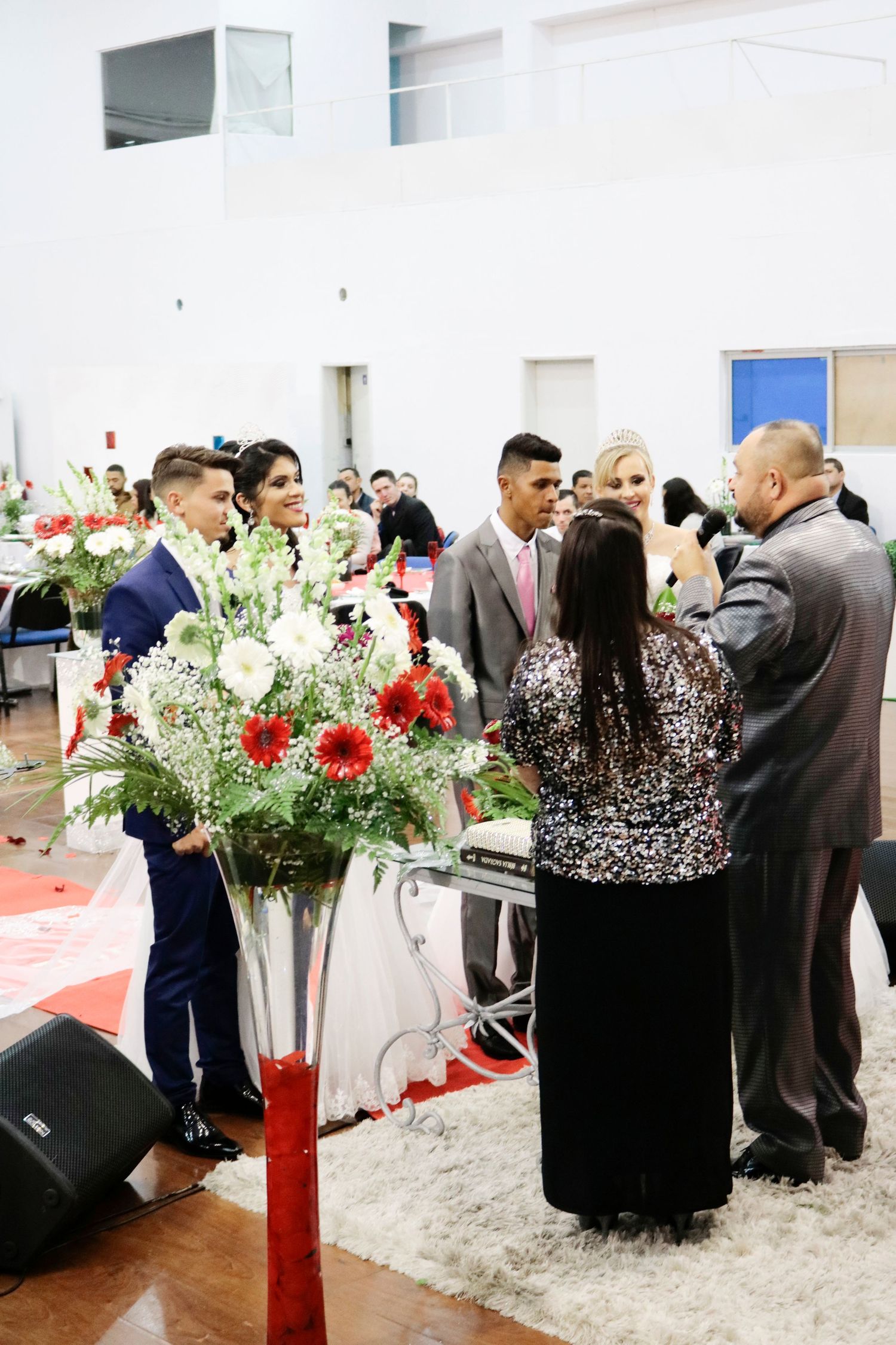 Reception venue decorated with red and white floral arrangements as guests mingle.