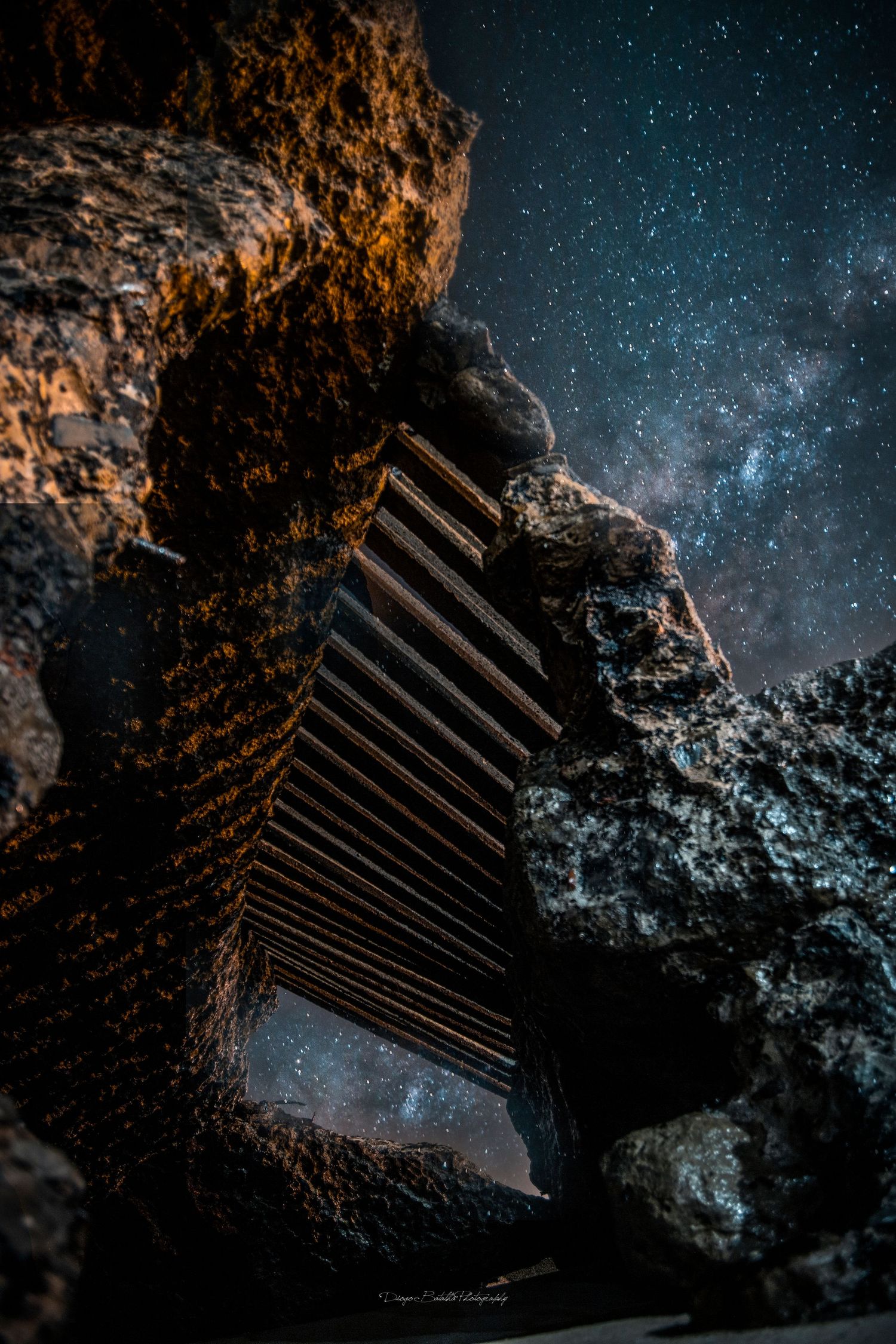A metal staircase inside a rocky cave formation against a starry night sky background.