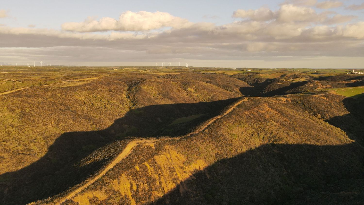 Rolling hills and valleys stretch across a rugged landscape under scattered clouds during golden hour.