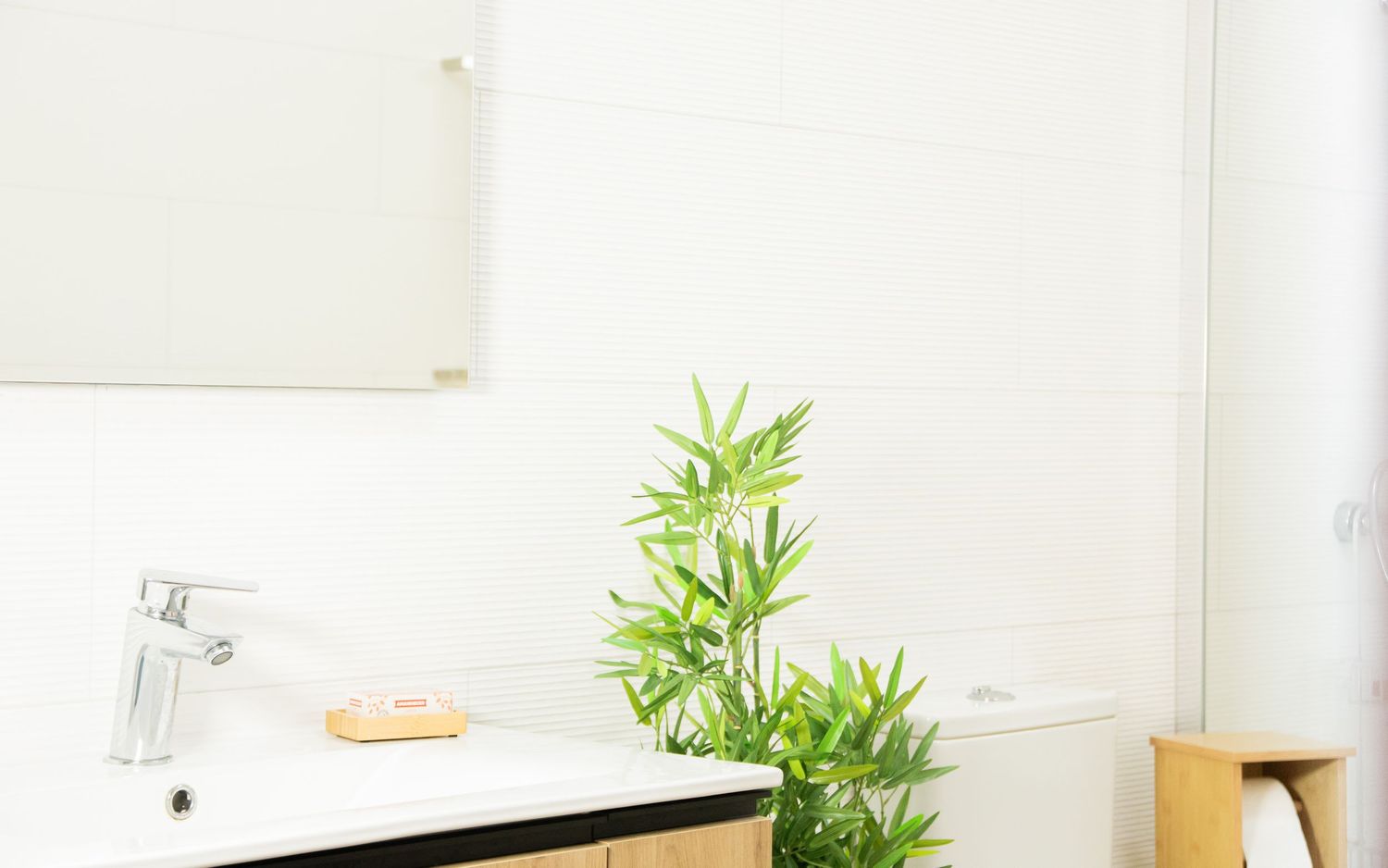 Modern white bathroom vanity with bamboo plant decoration and chrome faucet next to a mirror.