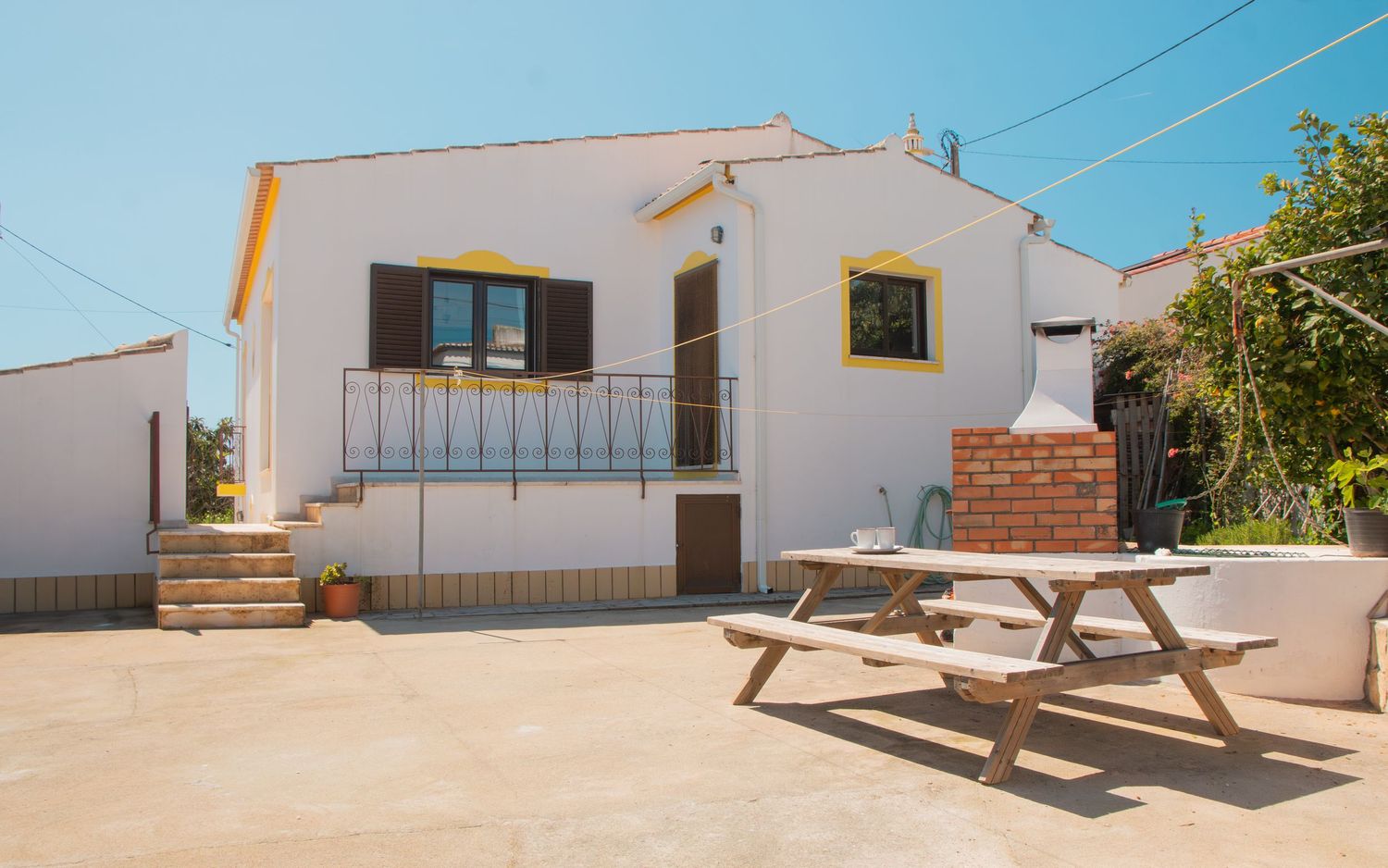White Mediterranean style villa with balcony and outdoor wooden picnic table on sunny terrace in Spain.