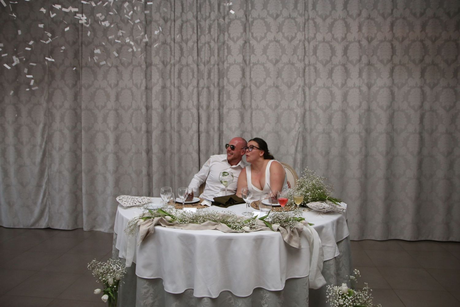 A couple sits at an elegantly decorated sweetheart table during their wedding reception.