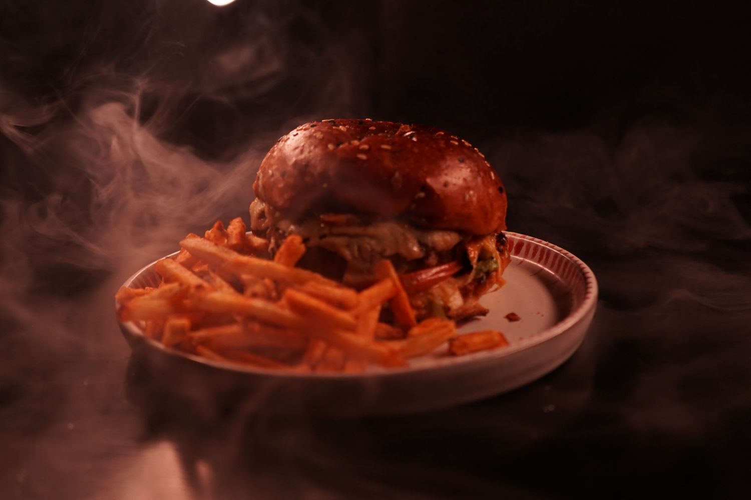Dramatic photo of a burger and fries on a plate surrounded by atmospheric smoke.