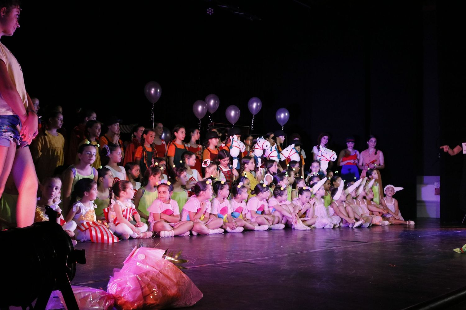 Dancers in tutus performing on stage during recital with dramatic stage lighting.