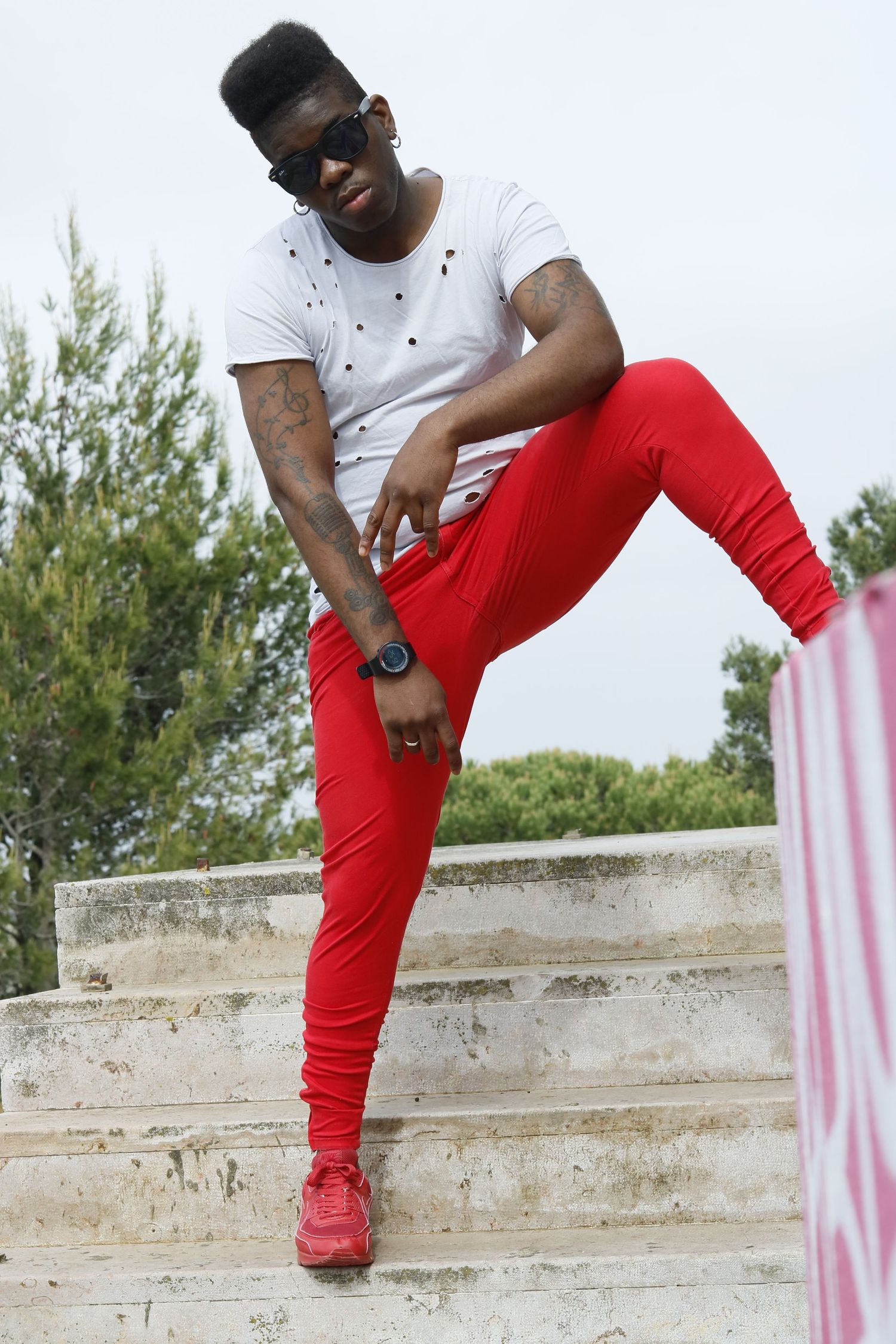 Person in casual streetwear outfit with white t-shirt, red pants and matching red sneakers poses on concrete steps outdoors.