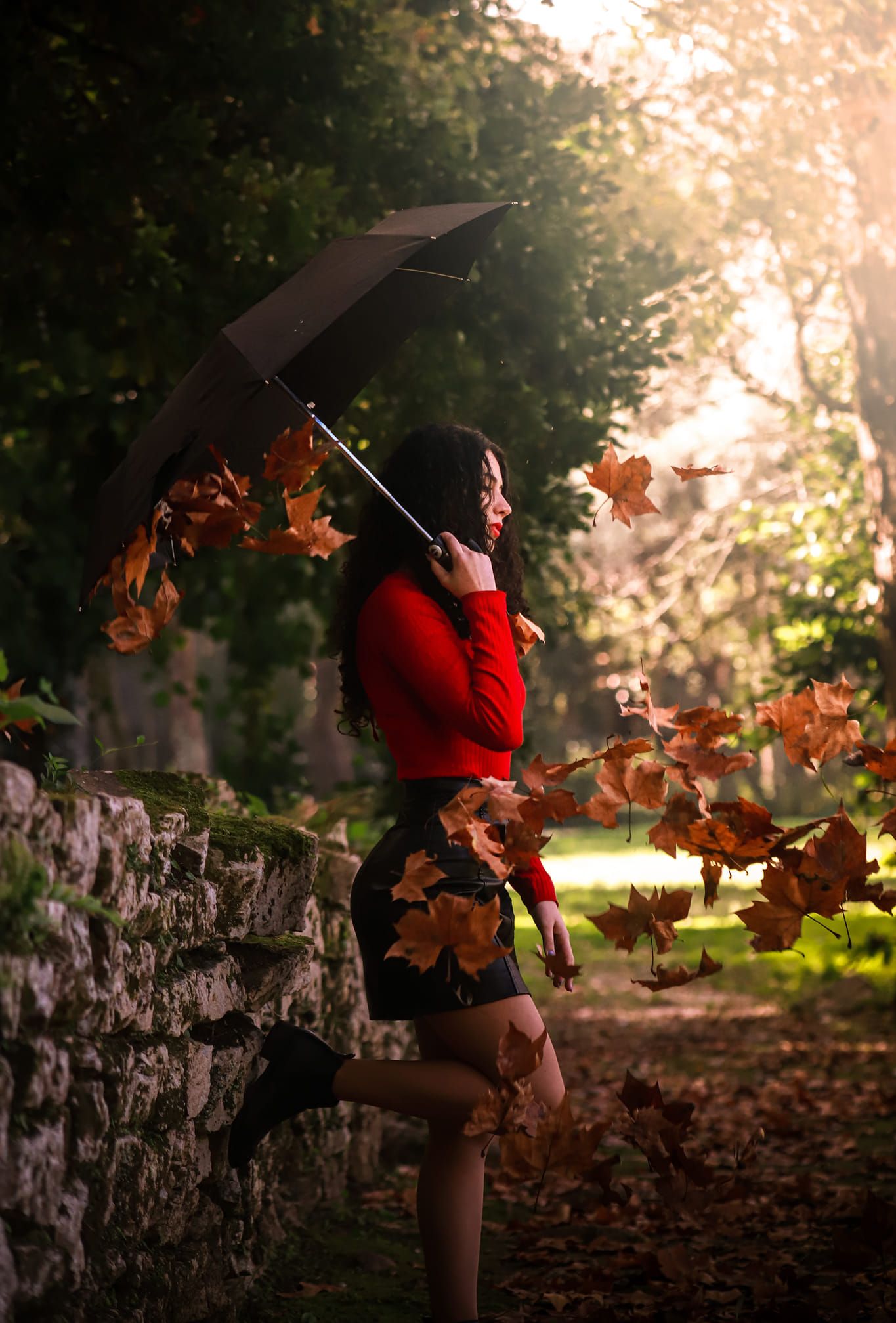 Autumn scene with person holding umbrella among falling leaves at sunset.