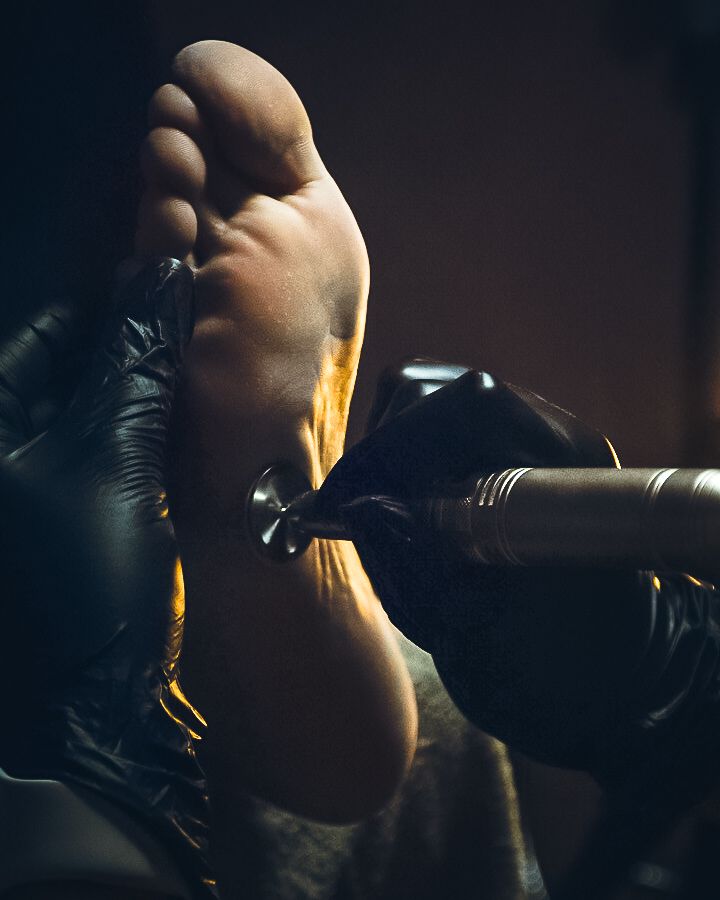 Closeup of tattoo artist wearing black gloves applying yellow ink to the sole of a client's foot during a tattoo session.