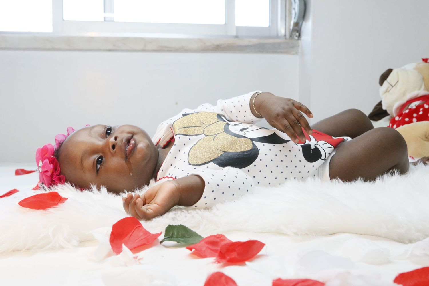 Baby in polka dot outfit lying on white blanket with red decorative elements.